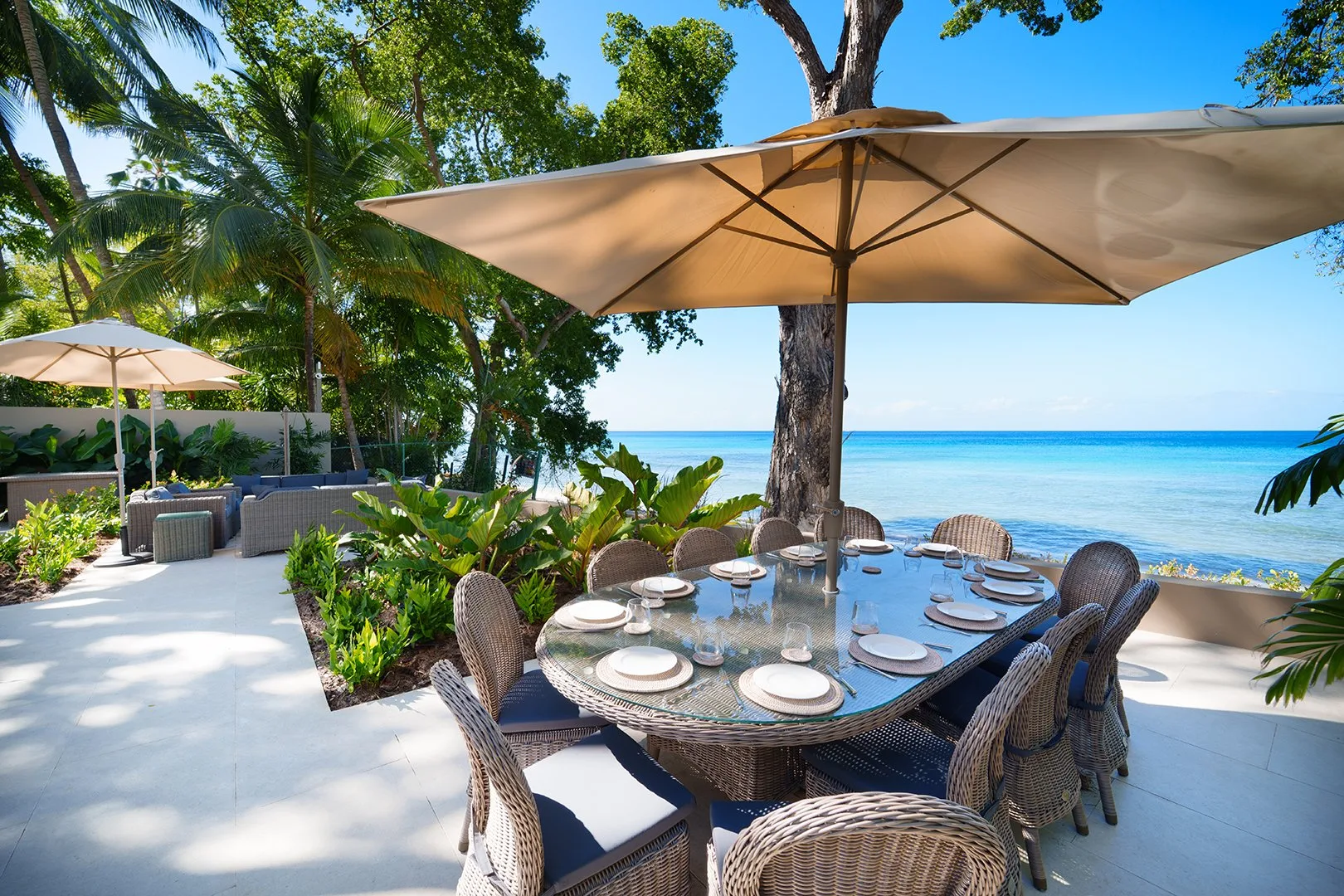 An outdoor dining table with chairs and umbrellas overlooks the sea.