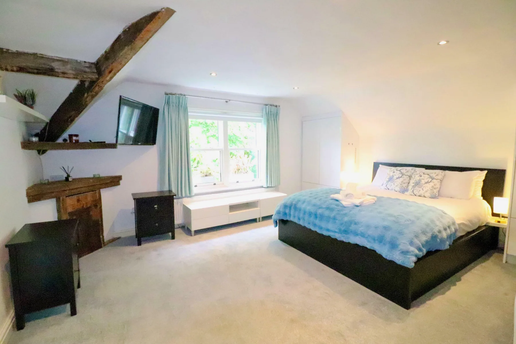 A bedroom with a bed, a window, and exposed ceiling beams.