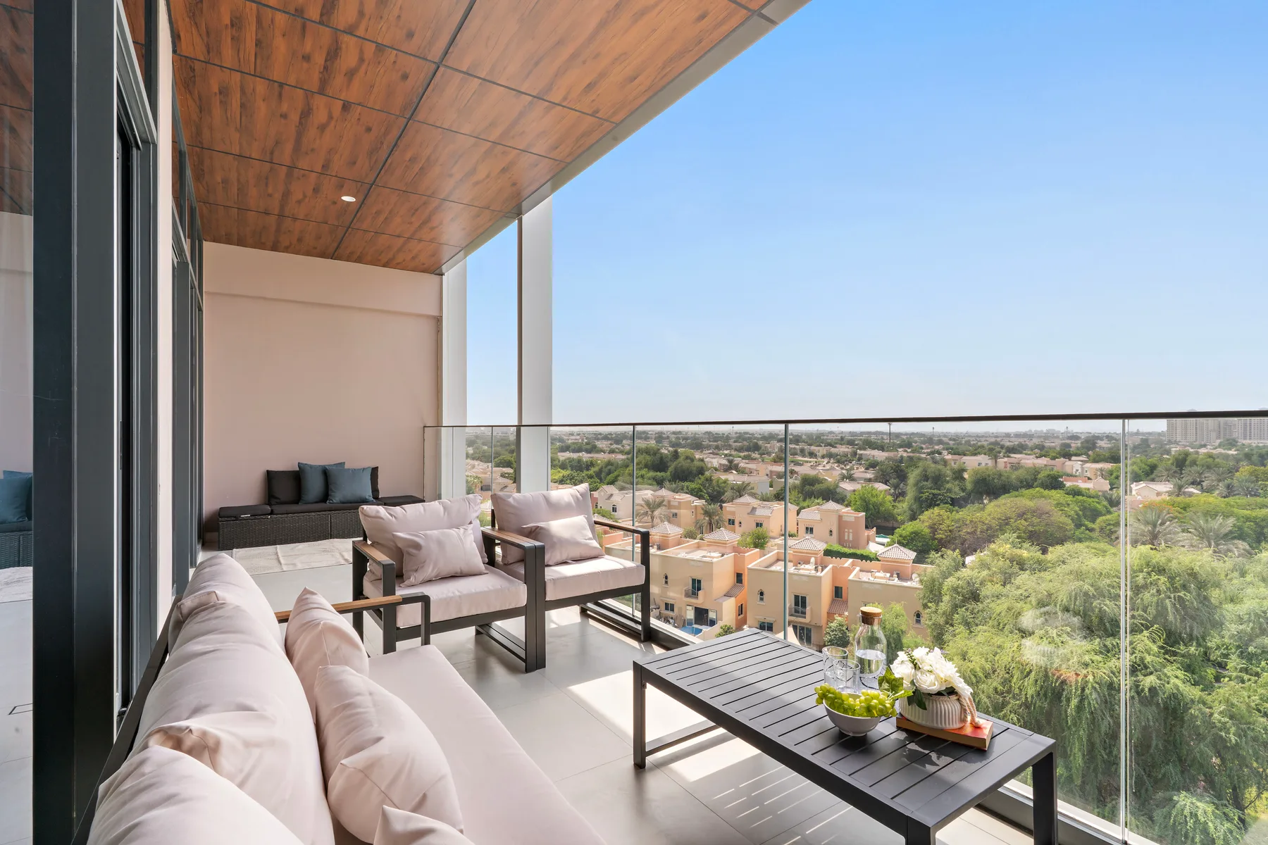 A covered balcony seating area overlooks a neighborhood and green trees.