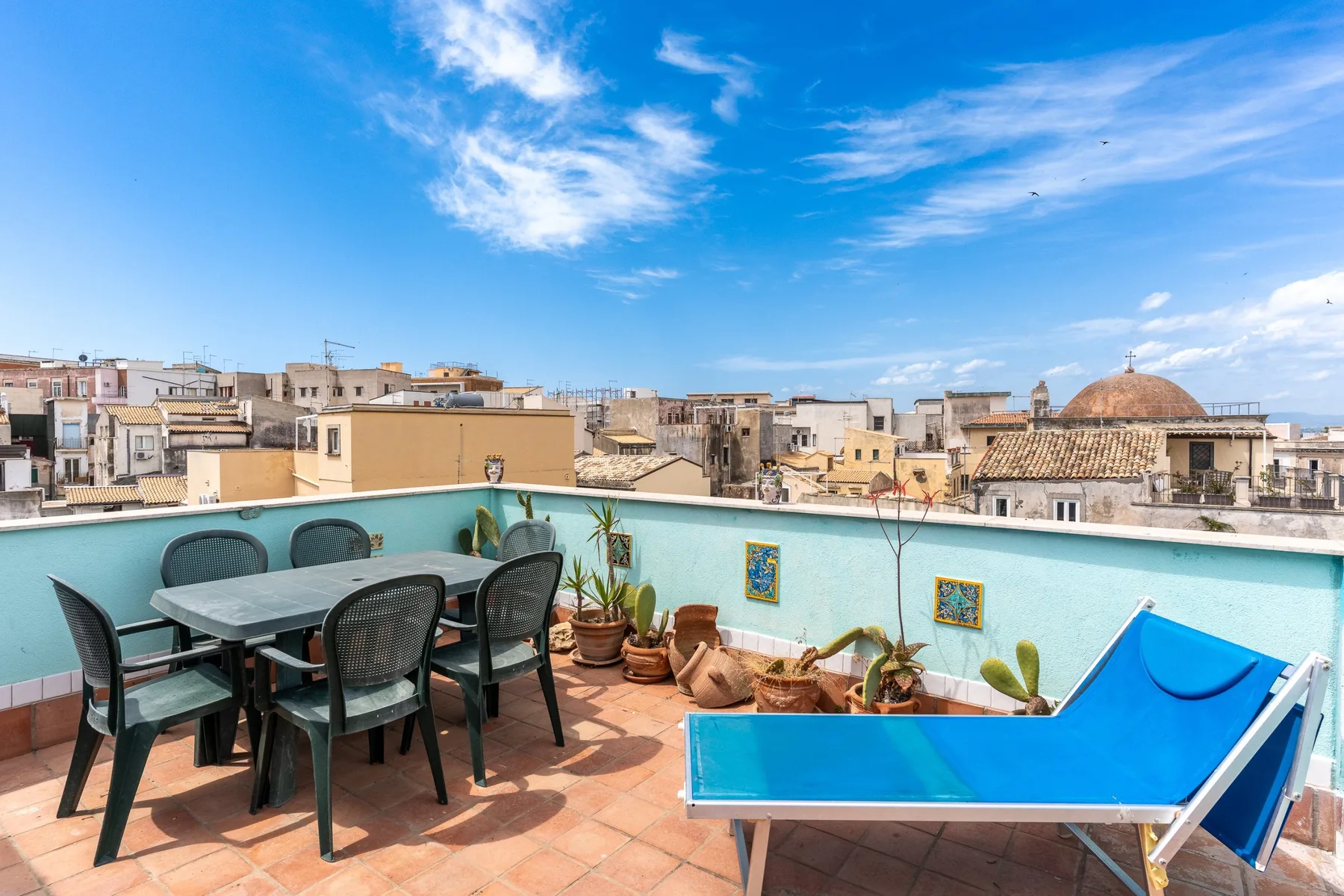 Una terraza en la azotea con asientos al aire libre, plantas en macetas y vistas a edificios cercanos.