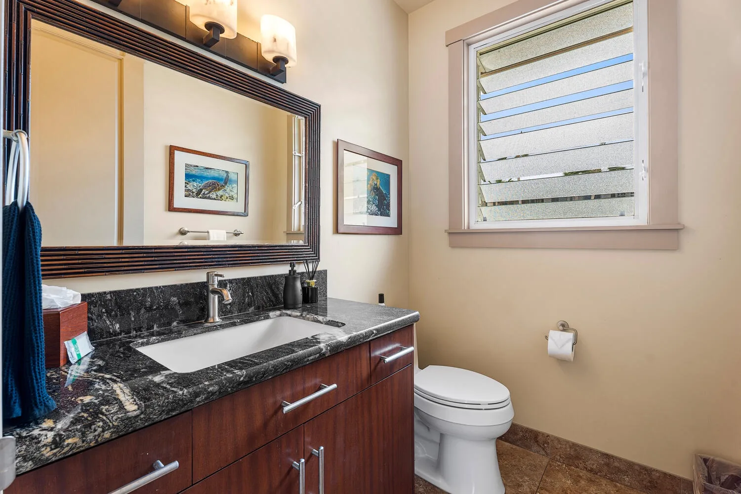 Un tocador de baño con espejo, lavabo e inodoro junto a una ventana de lamas.