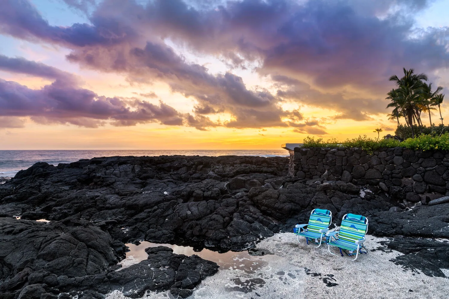 Una costa rocosa al atardecer, con dos sillas de playa junto al agua.