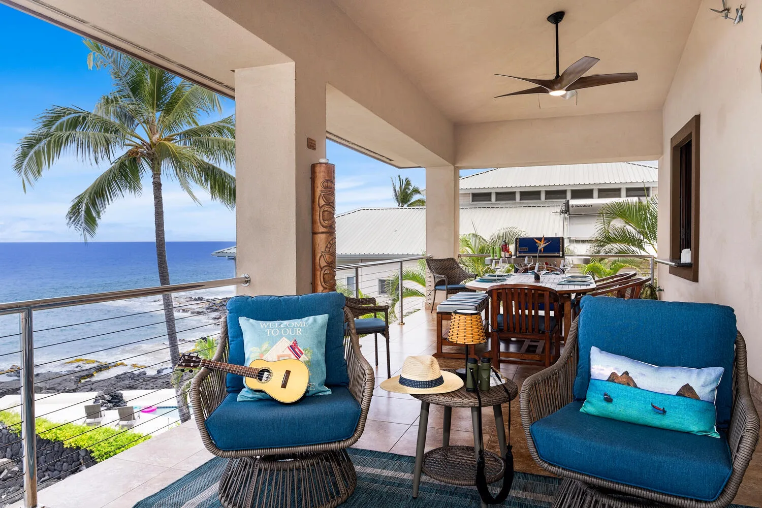 Un patio cubierto con asientos azules, una mesa de comedor y vista al mar.