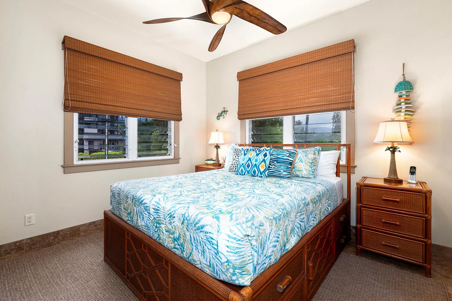 Un dormitorio con una cama estampada azul, mesitas de madera y ventanas con persianas.