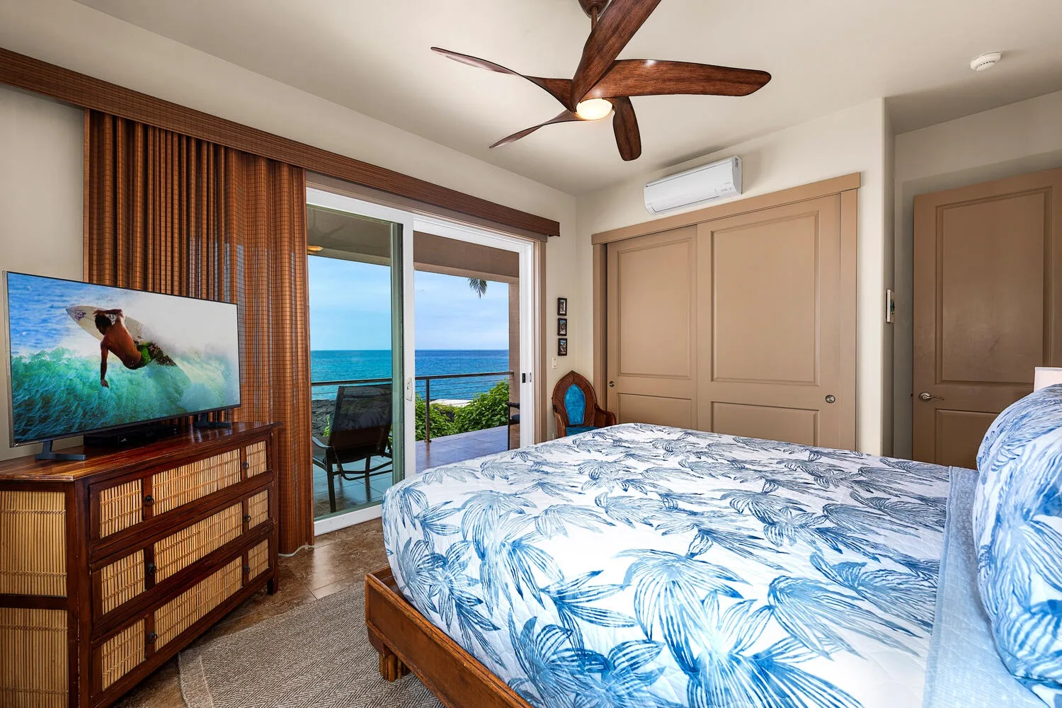 Un dormitorio con una cama cubierta con ropa de cama floral azul y una puerta corrediza de vidrio con vista al mar.