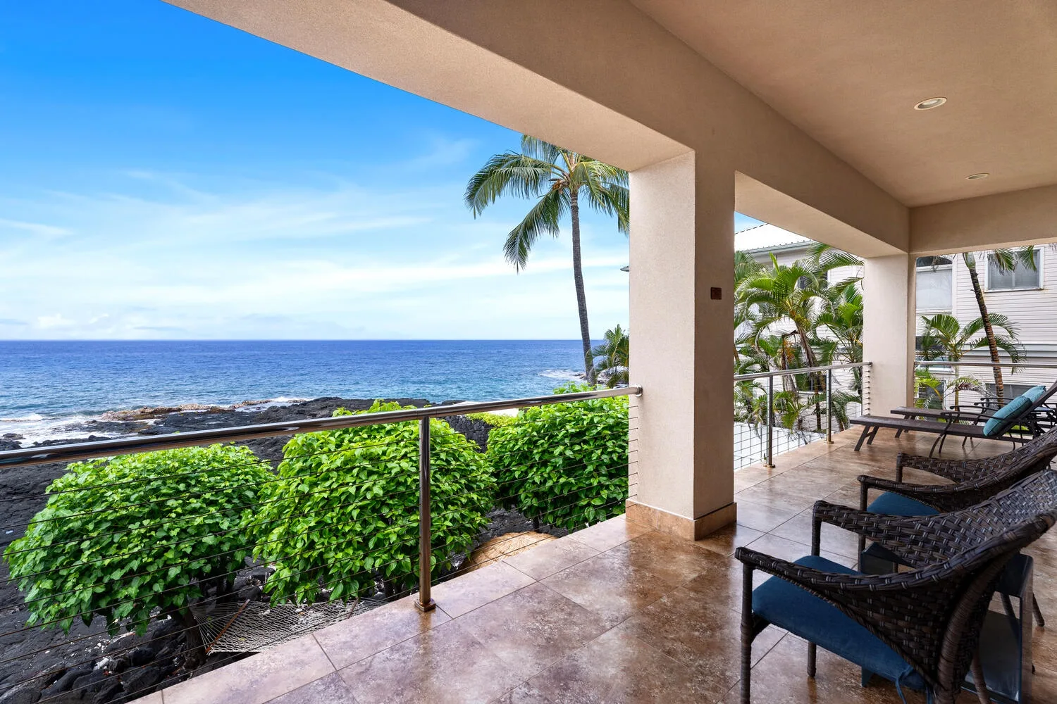 Una terraza cubierta junto al mar mira al océano, con asientos y plantas tropicales.