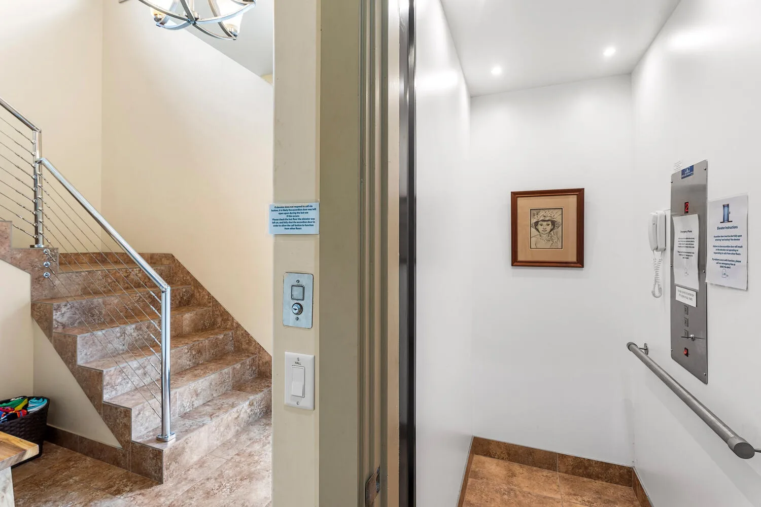Interior de un ascensor junto a una escalera, con una obra enmarcada en la pared.