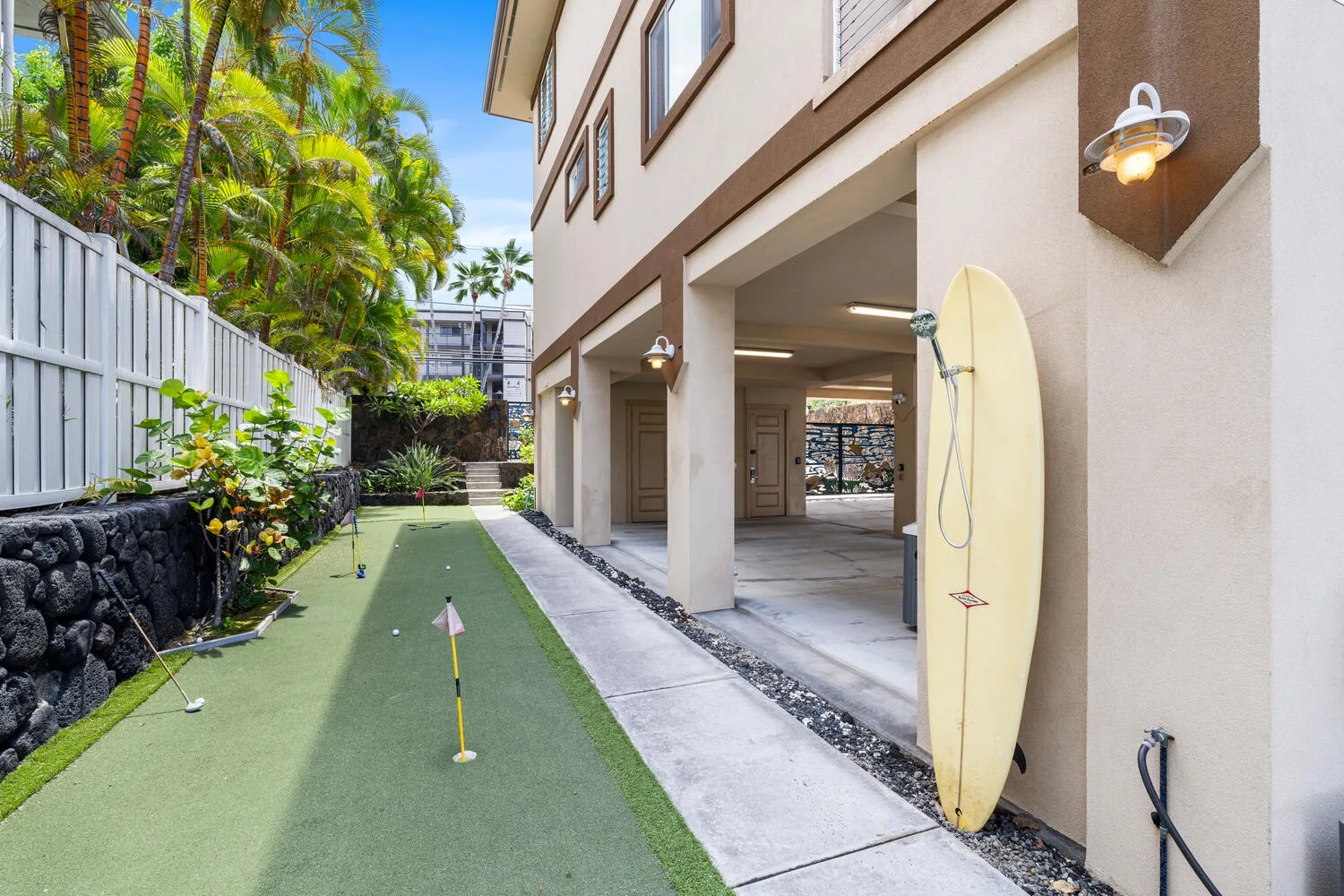 Una zona exterior para practicar golf junto al edificio, con una tabla de surf apoyada en la pared.