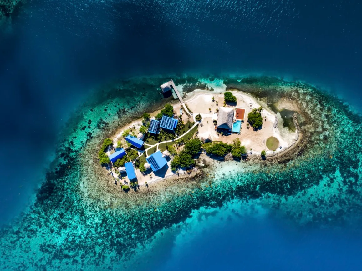 An aerial view of a small island surrounded by turquoise water and coral reef.