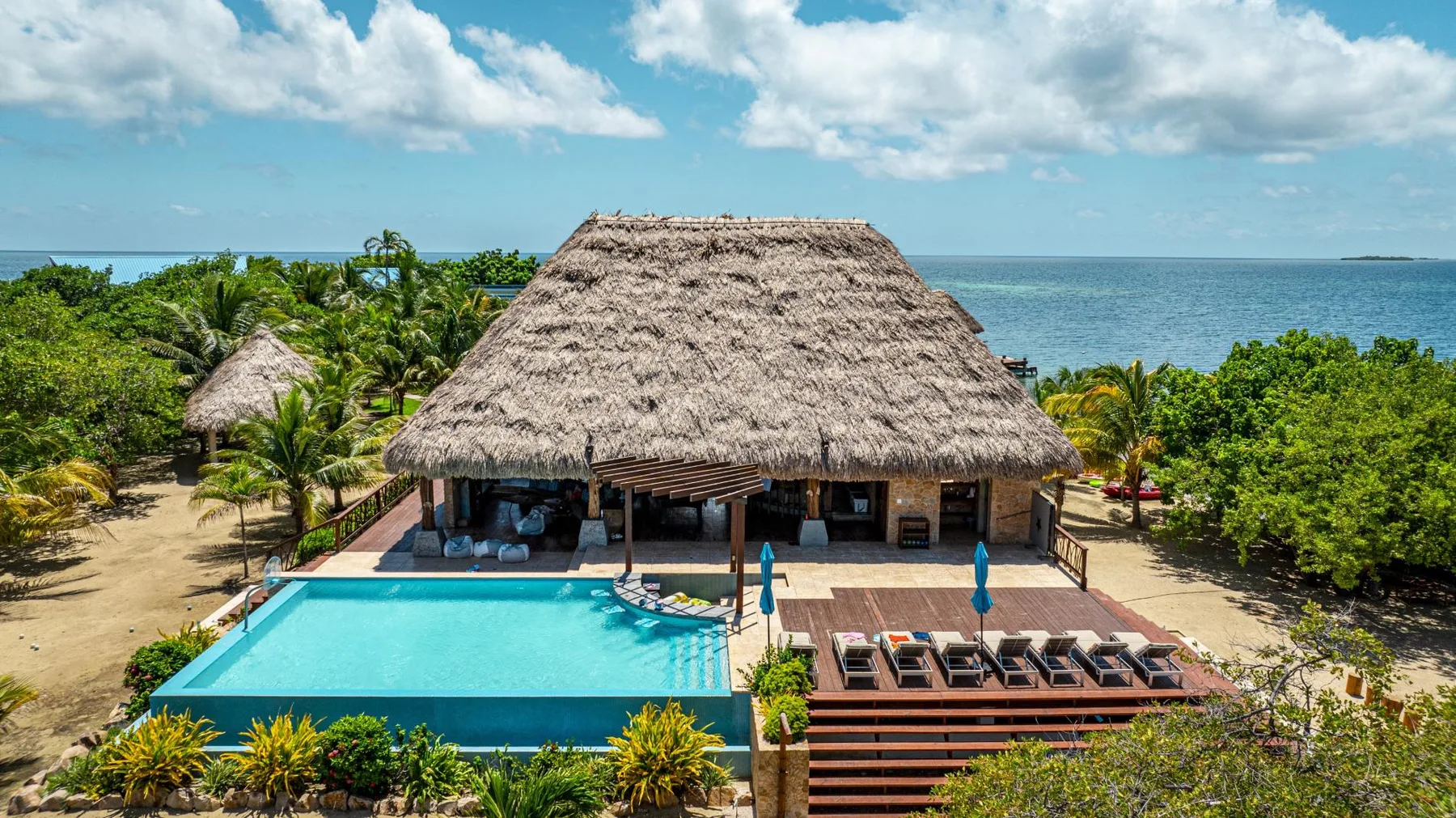 A thatched-roof pavilion stands beside a turquoise pool overlooking the sea.