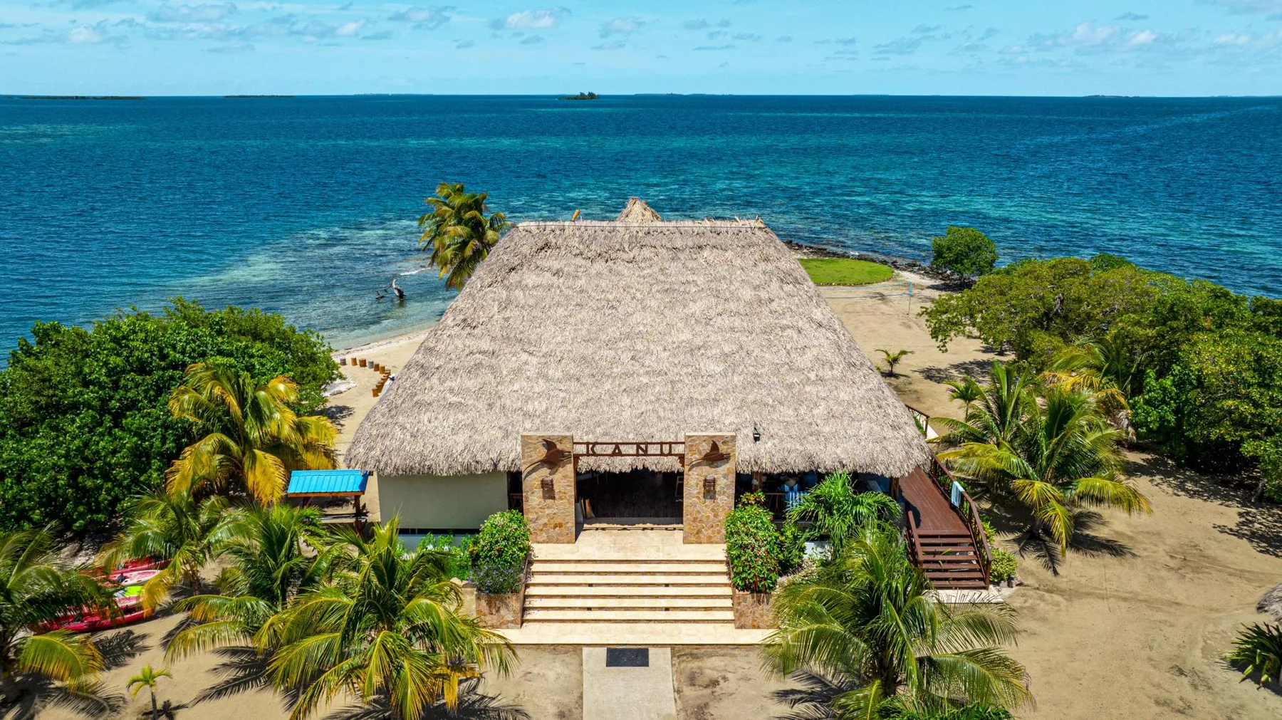 A thatched-roof pavilion stands among palm trees beside the turquoise sea.