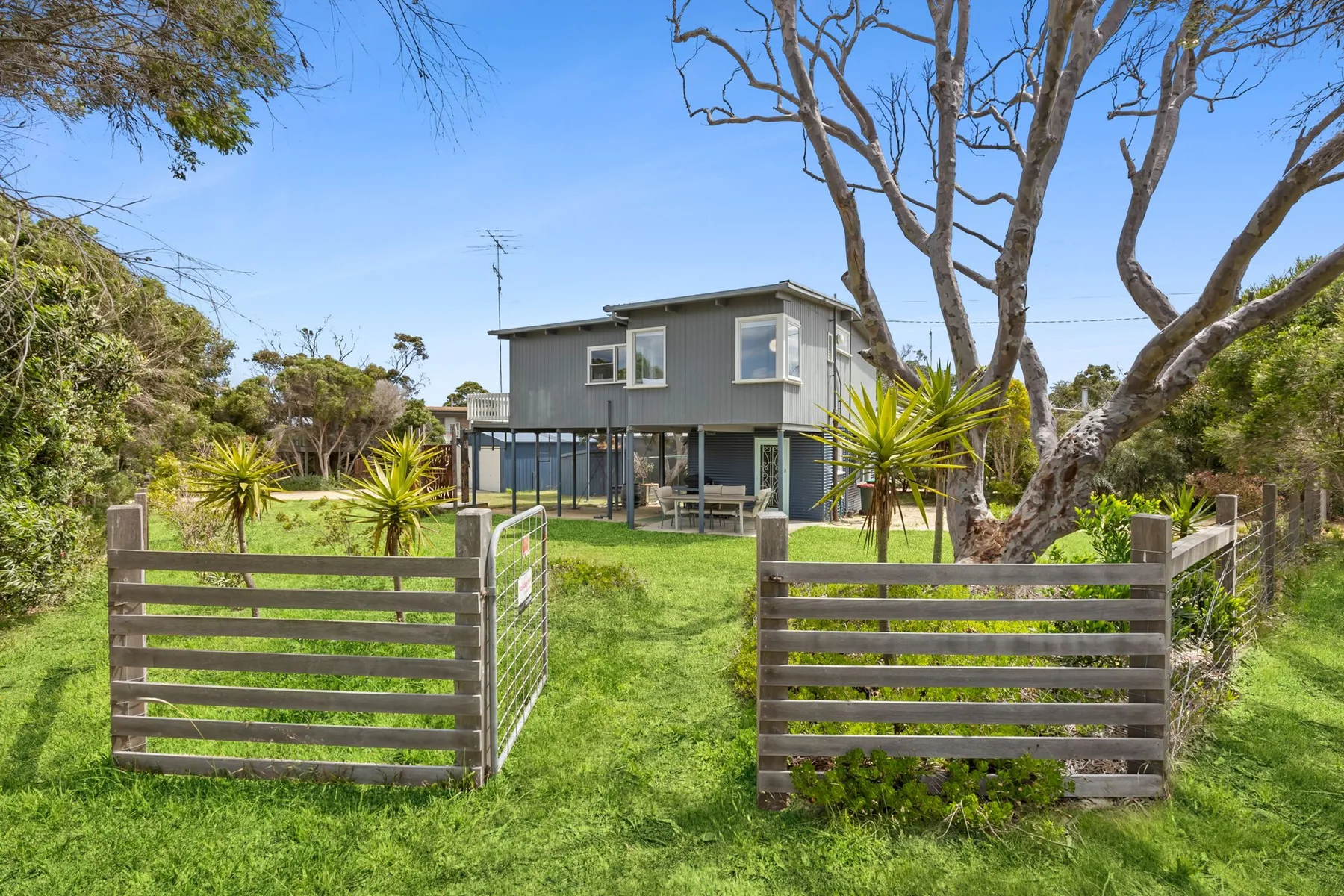 A two-story house stands beyond a grassy yard with a wooden gate.