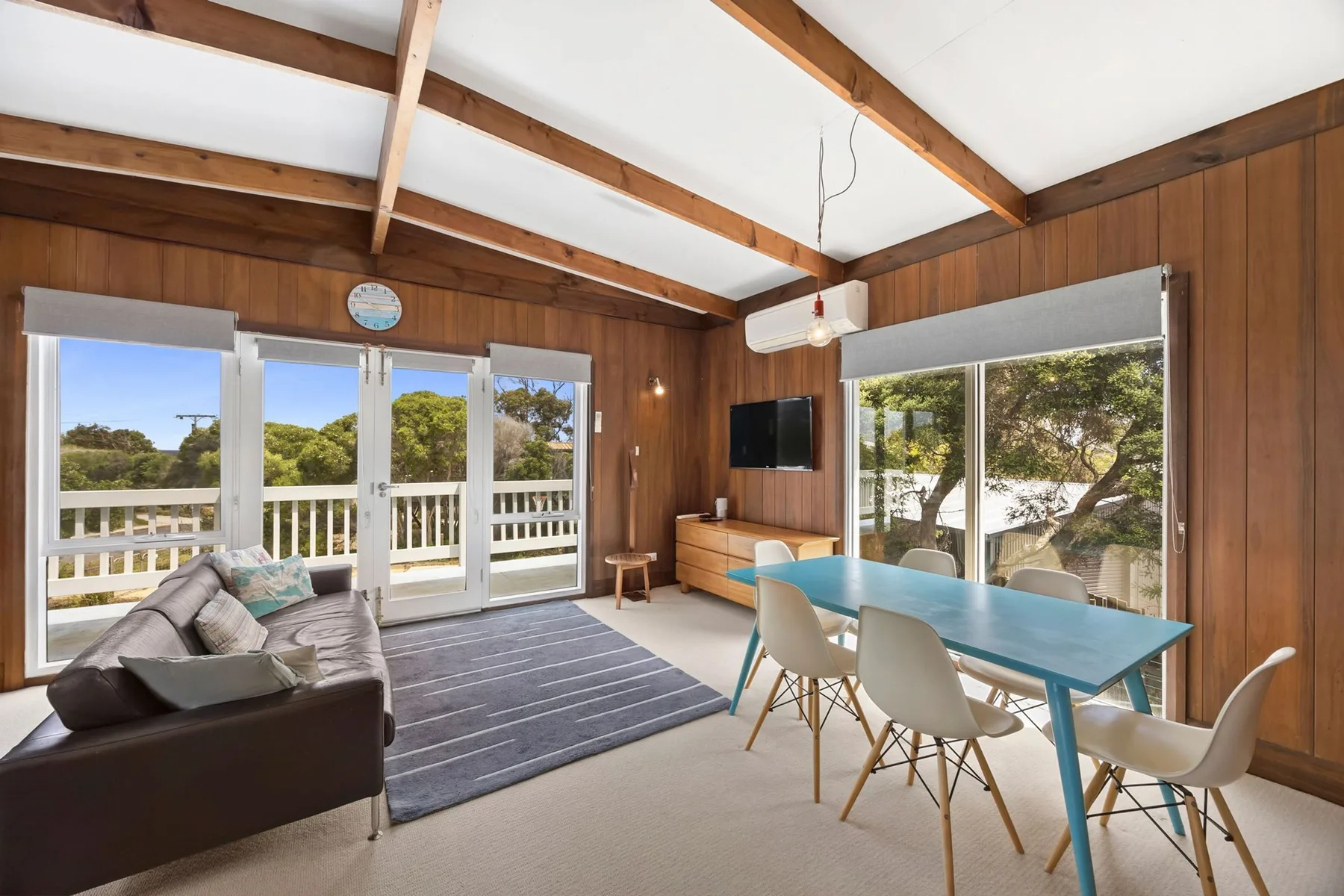 A living and dining area with wood-paneled walls and large windows.