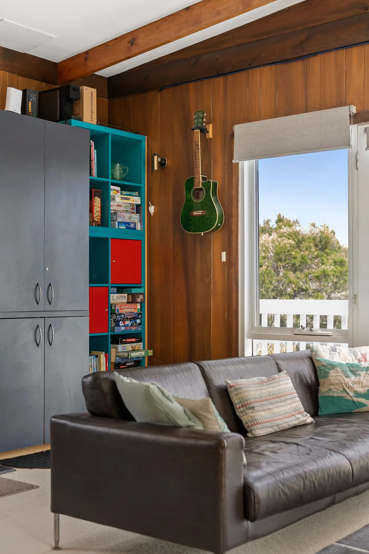 A wood-paneled living room with a guitar on the wall and seating by a window.