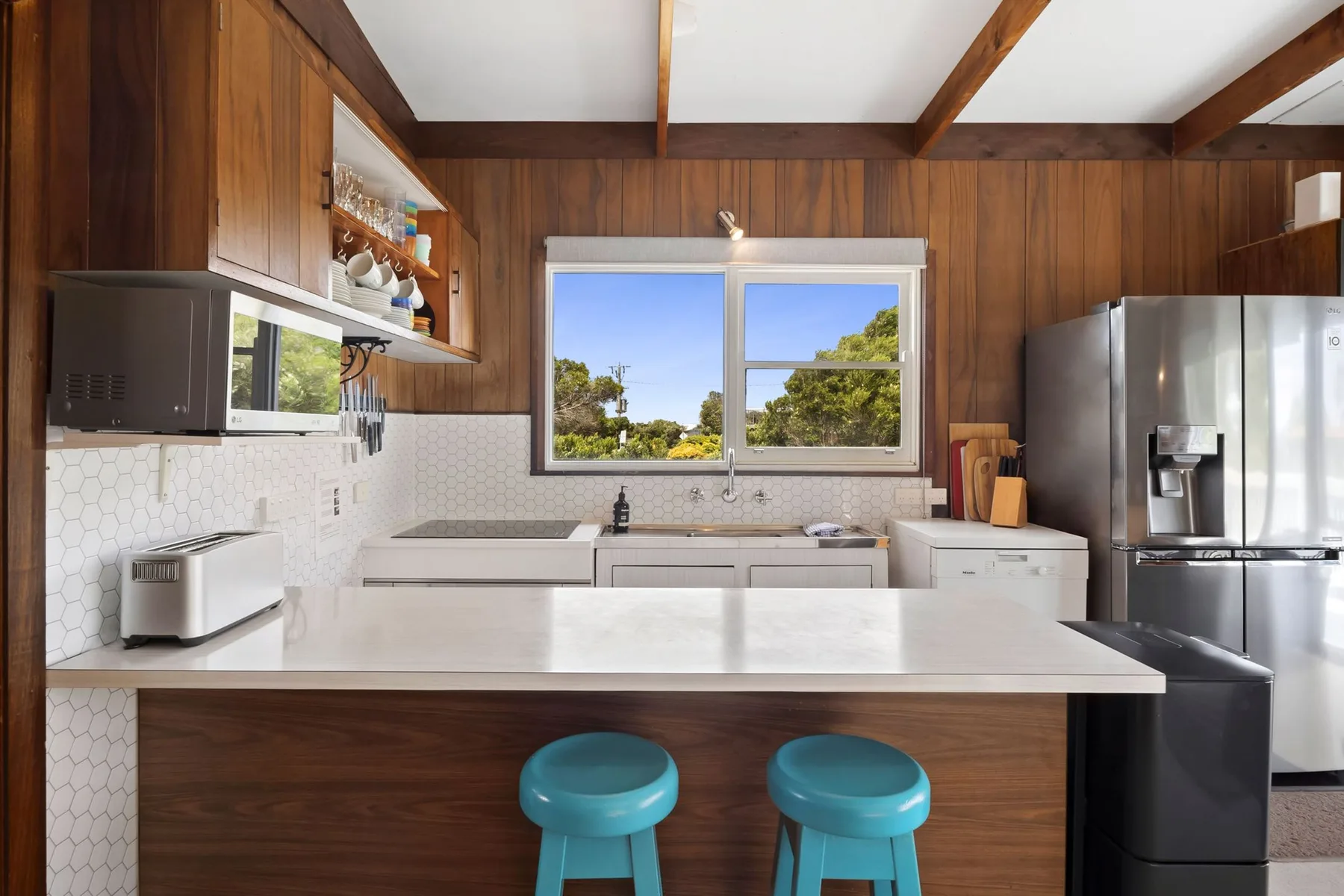 Una cocina con una isla amplia y dos taburetes azules bajo una ventana.