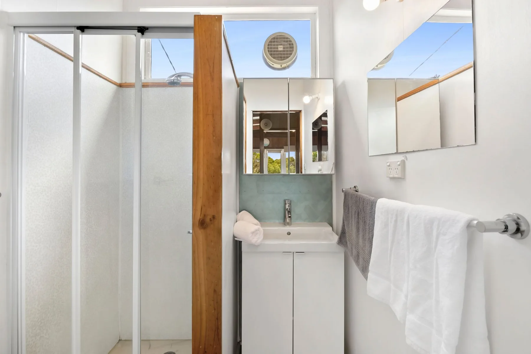 A bright bathroom with a sink, mirror, and glass shower.