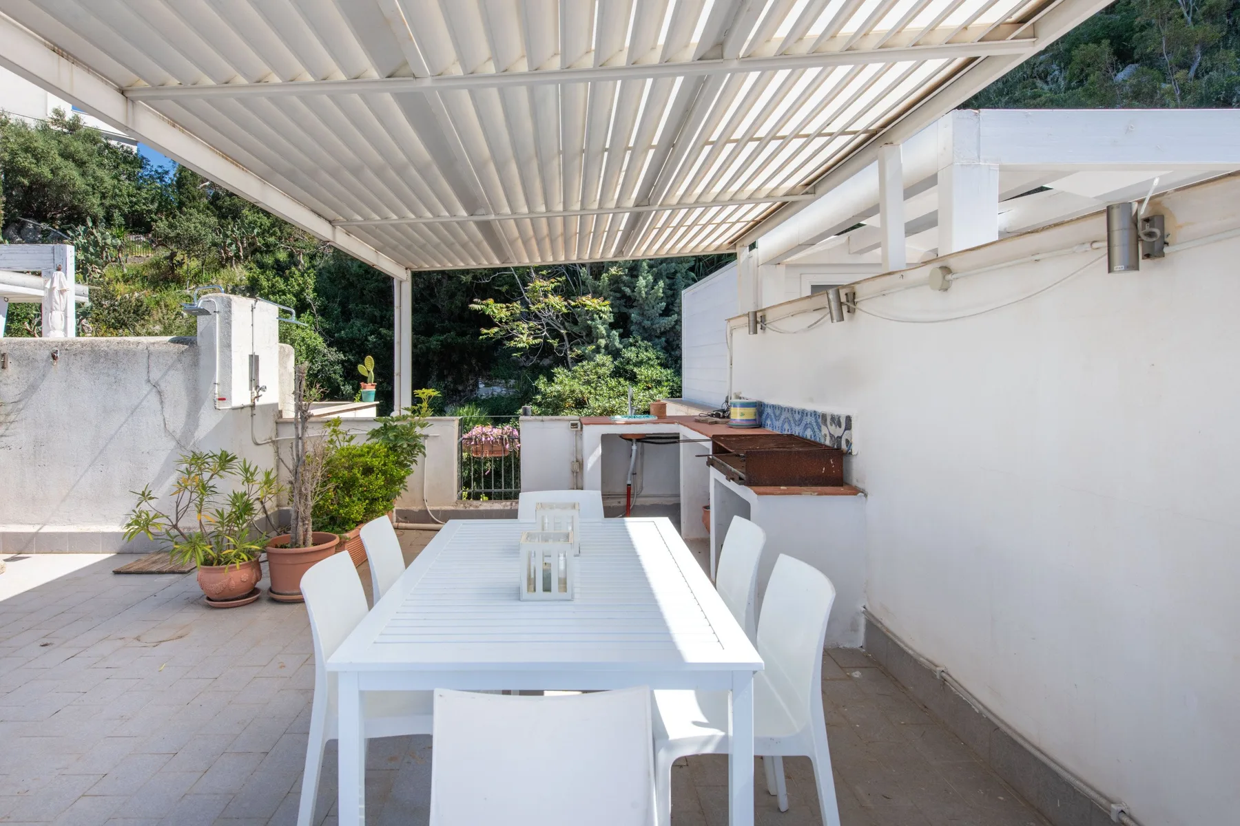 A covered outdoor dining area with a white table and kitchen counter.