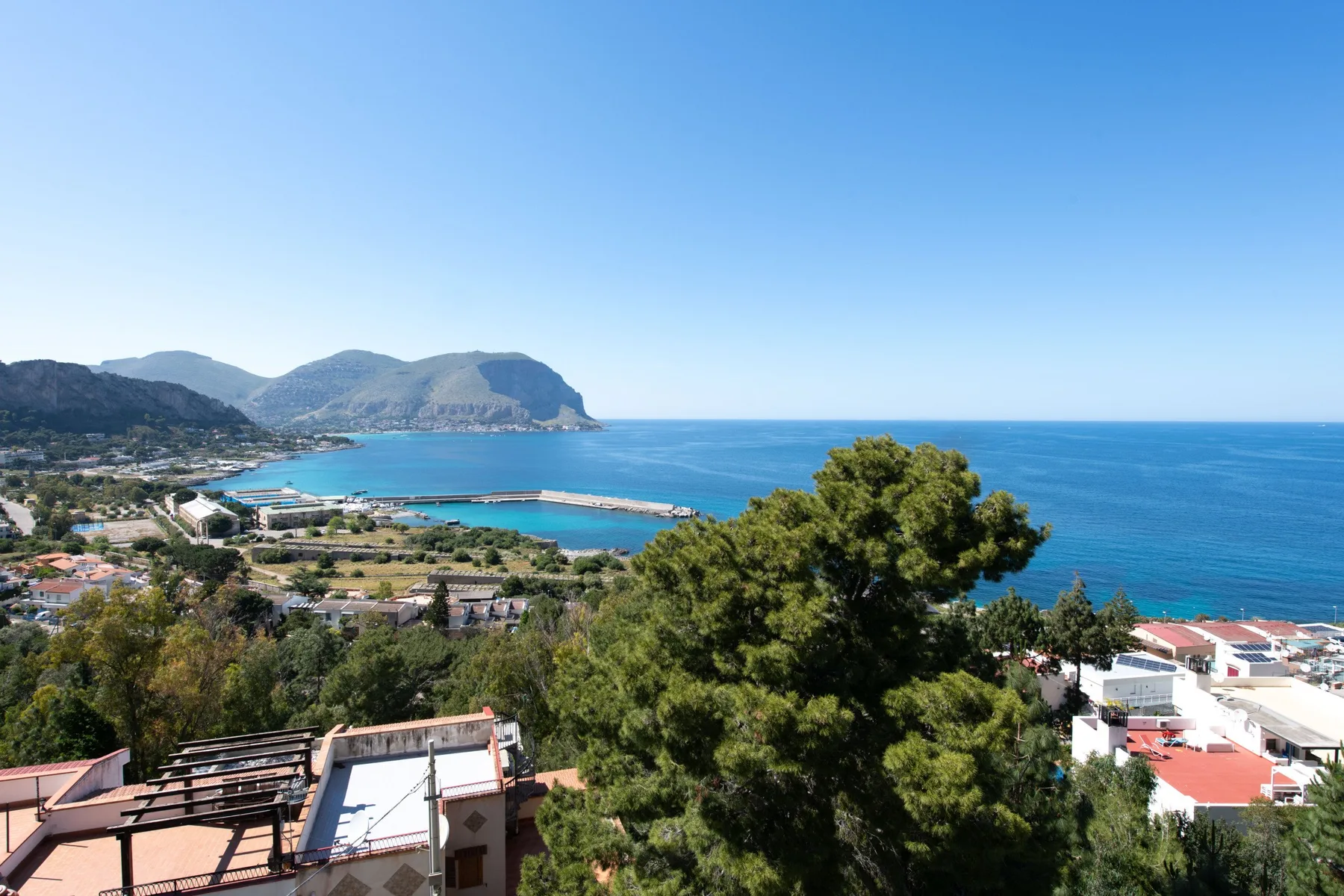 A coastal town and blue sea are visible beyond trees and rooftops.