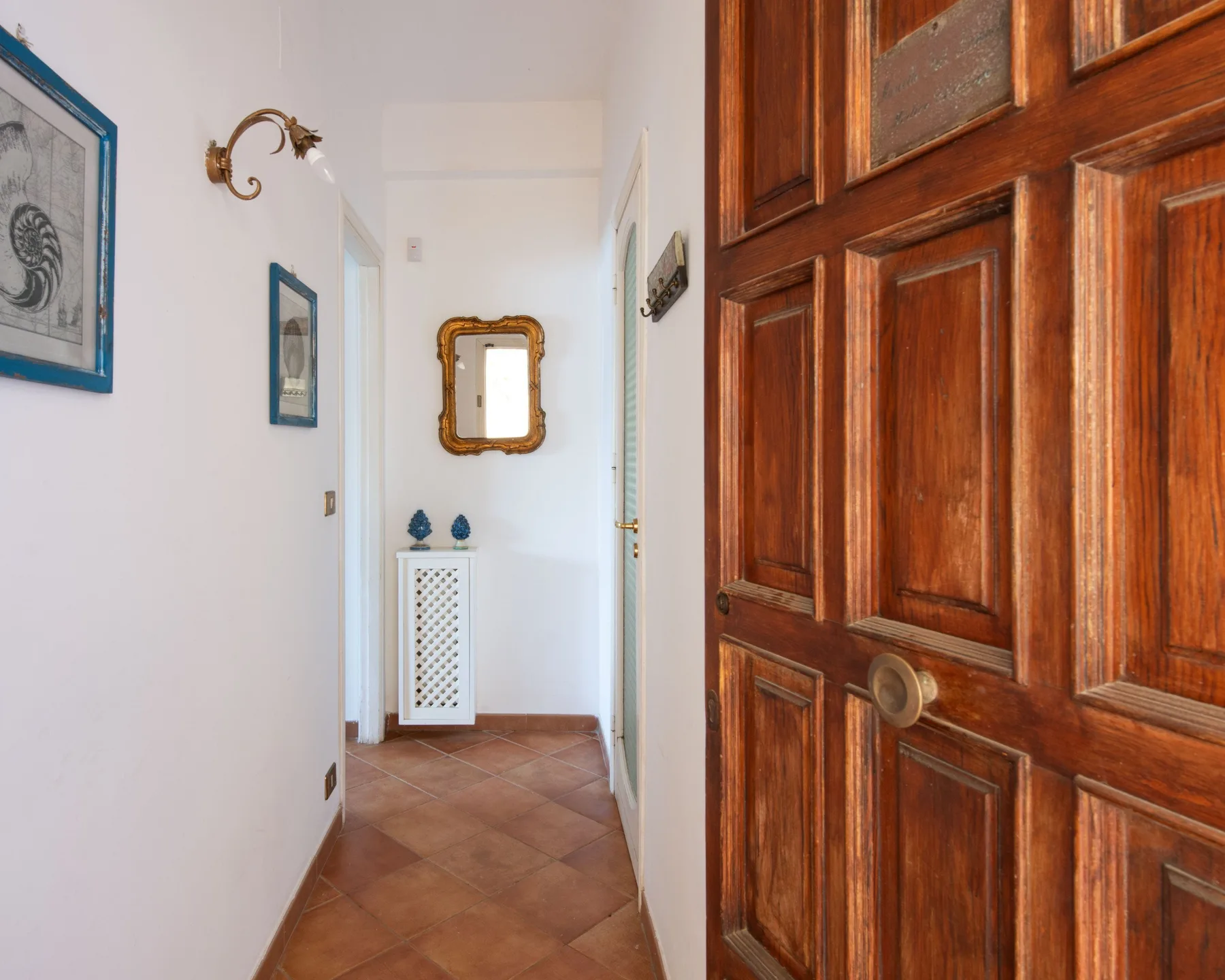 A narrow interior hallway with a wooden paneled door and framed pictures.