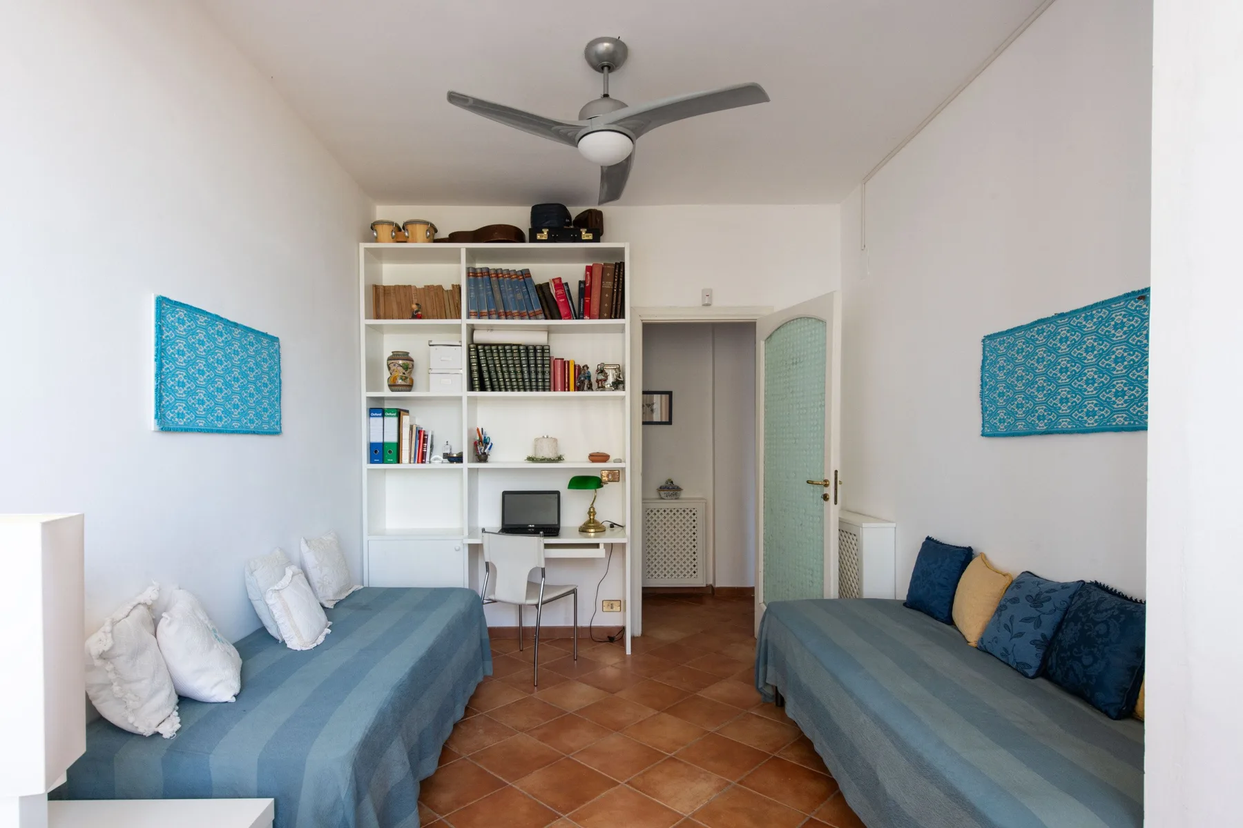 A bedroom with two beds, a bookshelf, and a ceiling fan.