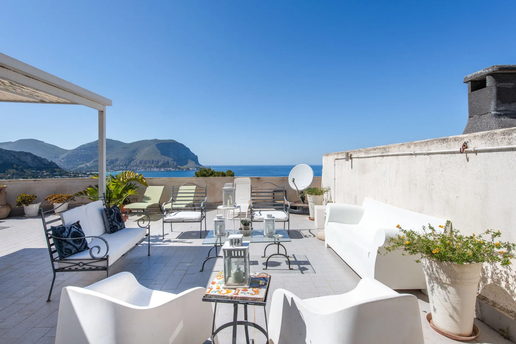 A rooftop terrace with outdoor seating and views of the sea and mountains.