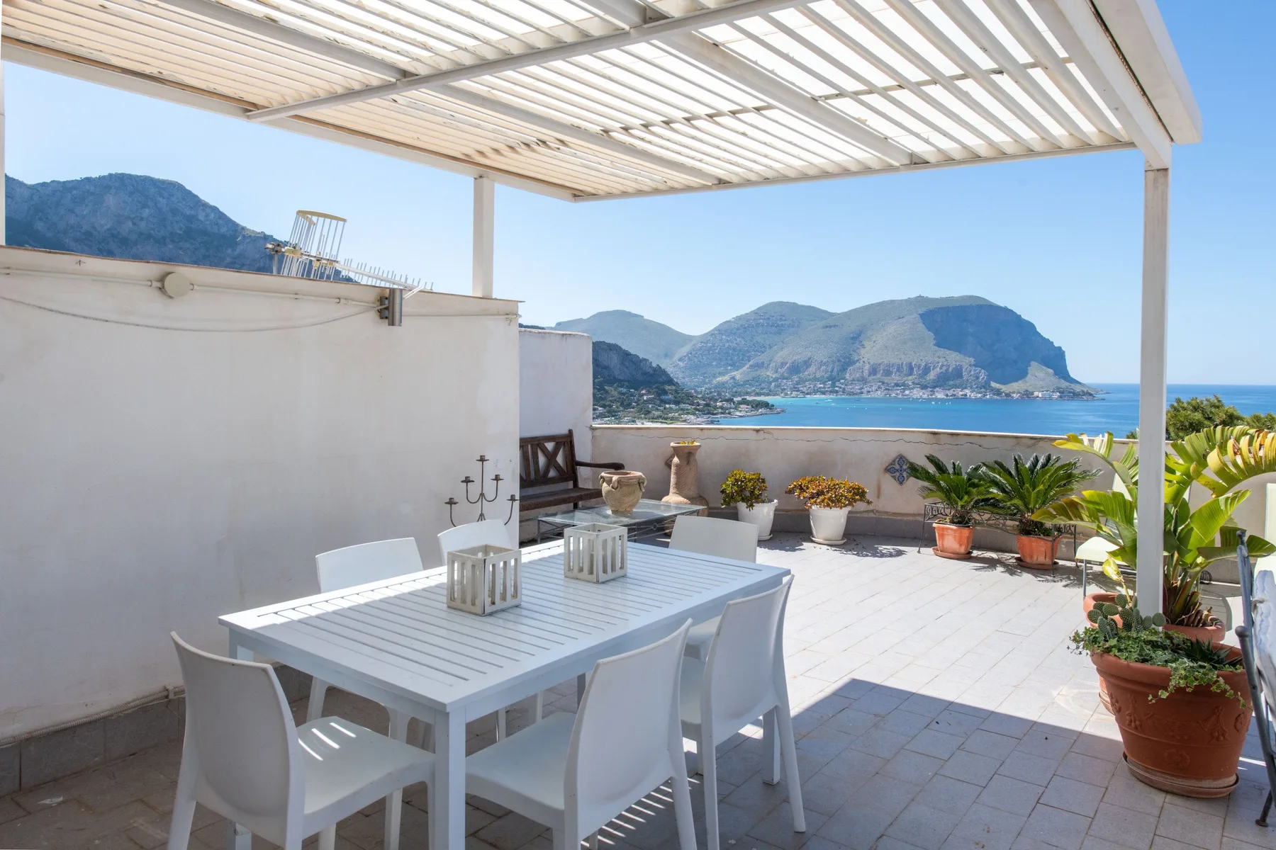 A sunlit terrace with outdoor seating and a view of the sea and mountains.