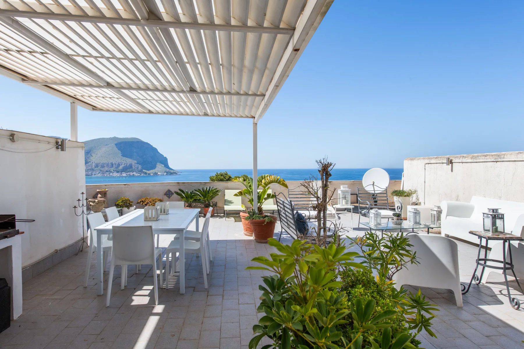 A seaside terrace with outdoor seating and potted plants overlooking the water.