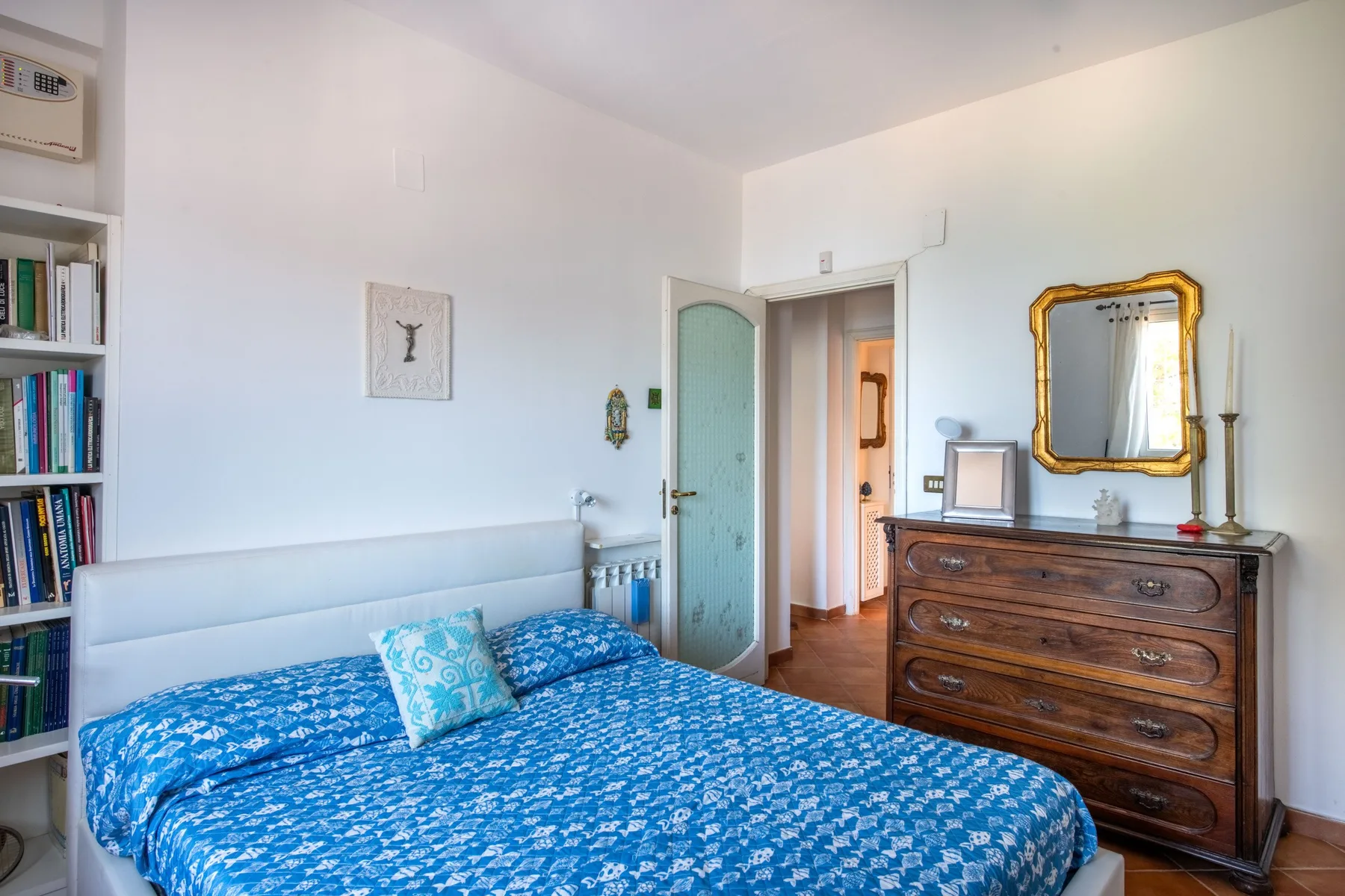 A bedroom with a blue patterned bedspread and a wooden dresser.