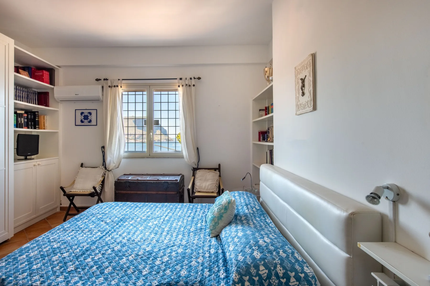 A bedroom with a blue patterned bedspread and a window with curtains.