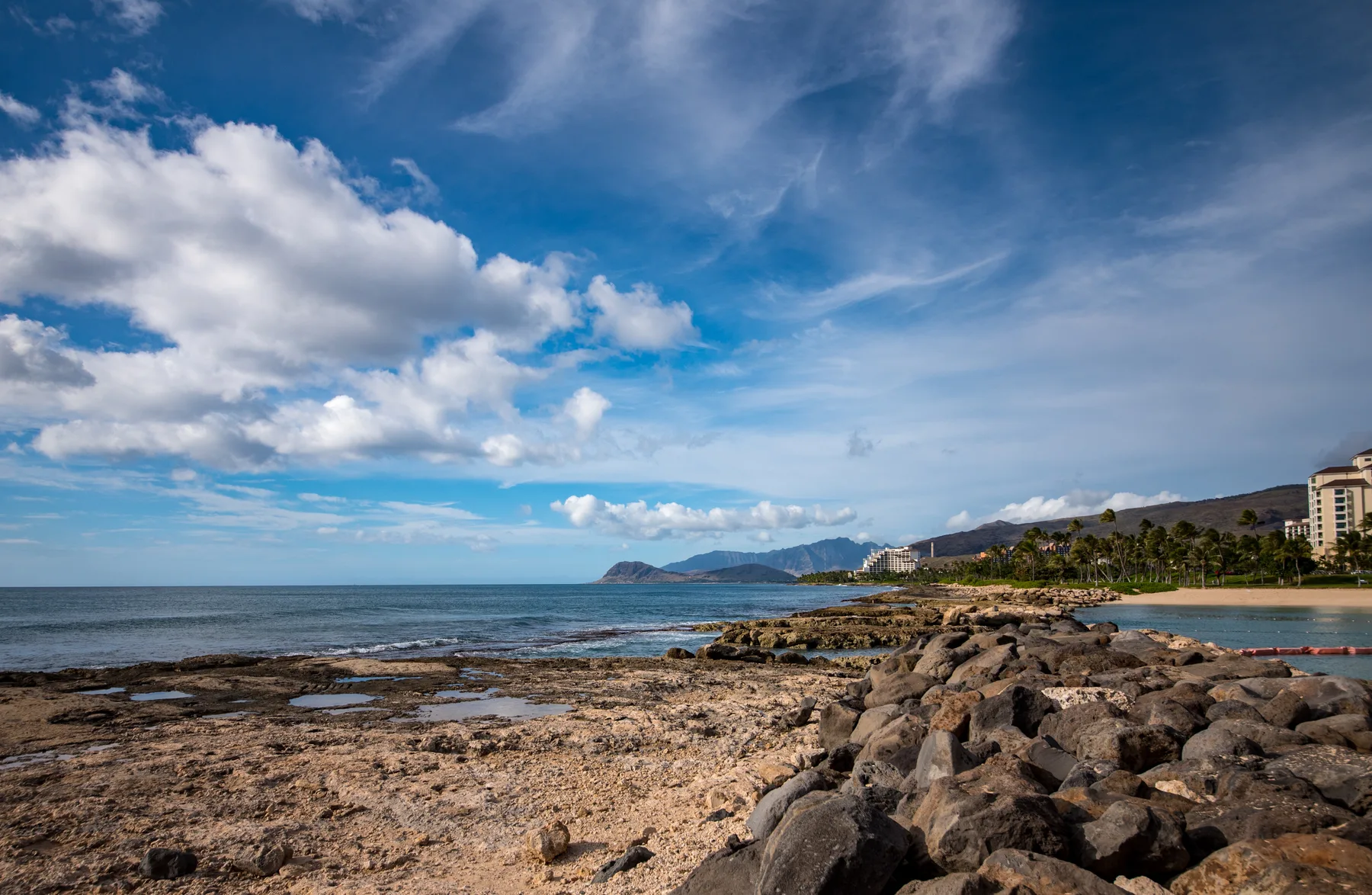 A rocky shoreline meets calm water beneath a broad, cloud-filled sky.