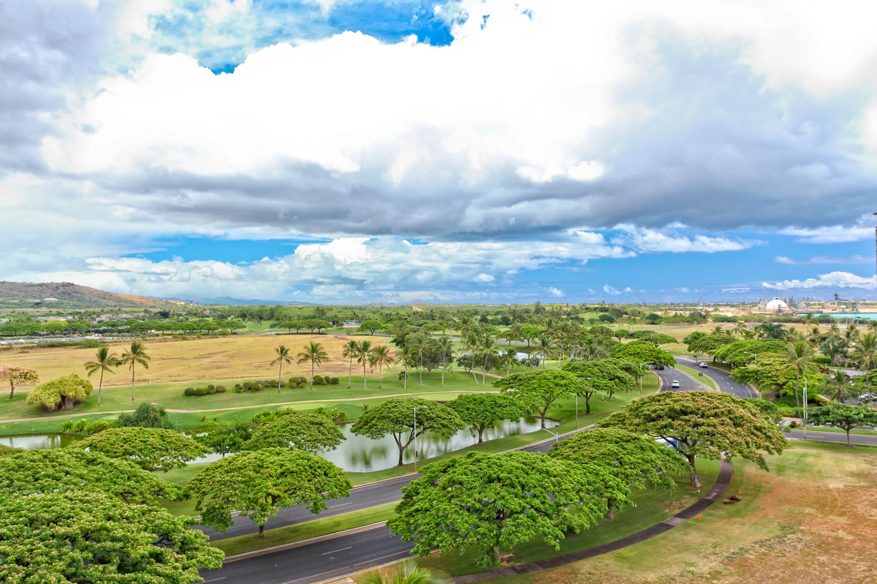 A landscaped park with green lawns, trees, and a pond beneath a cloudy sky.