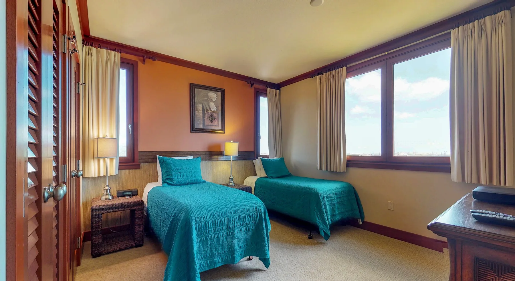 A bedroom with two beds dressed in teal and large curtained windows.