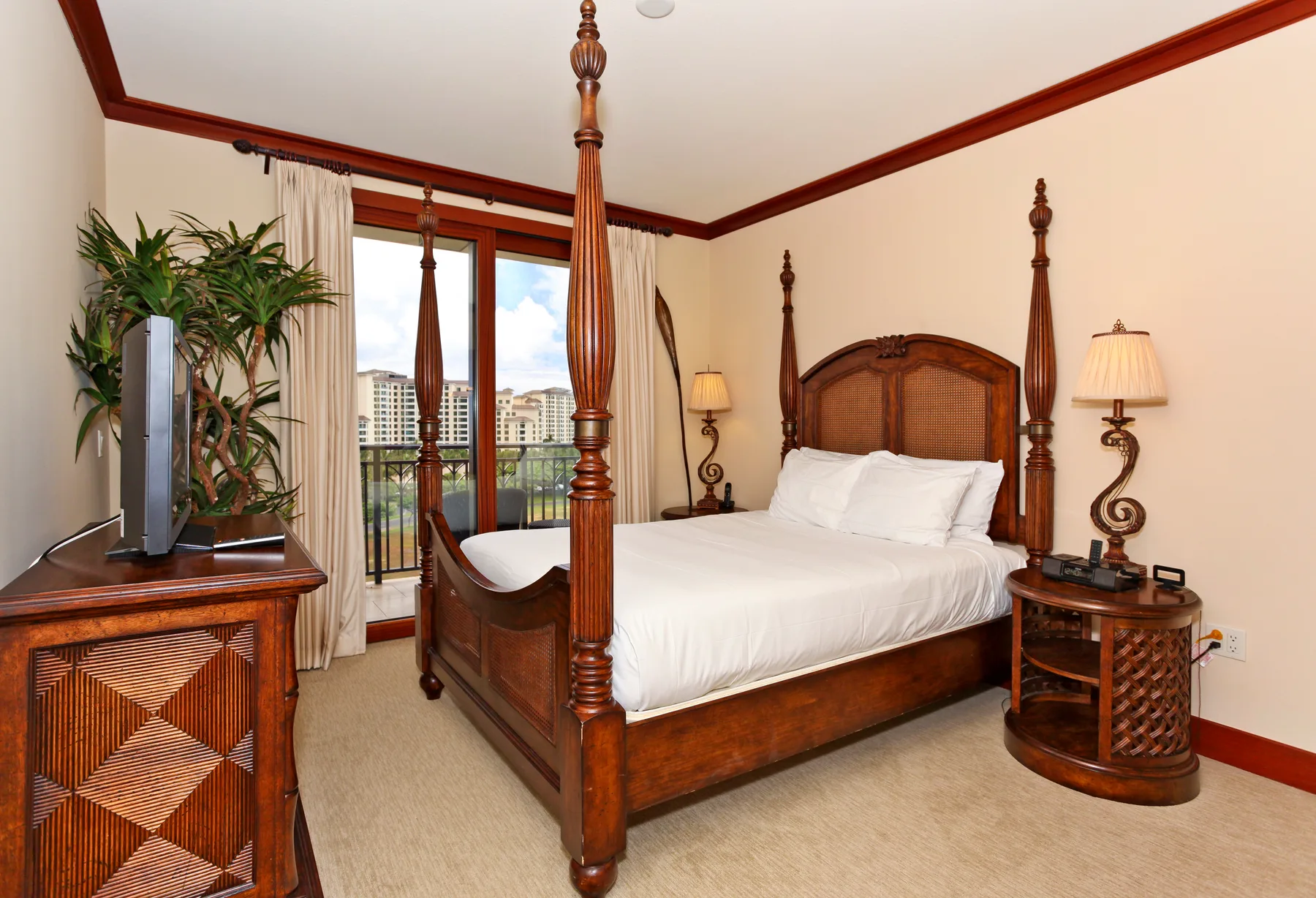 A bedroom with a wooden four-poster bed and glass doors to a balcony.