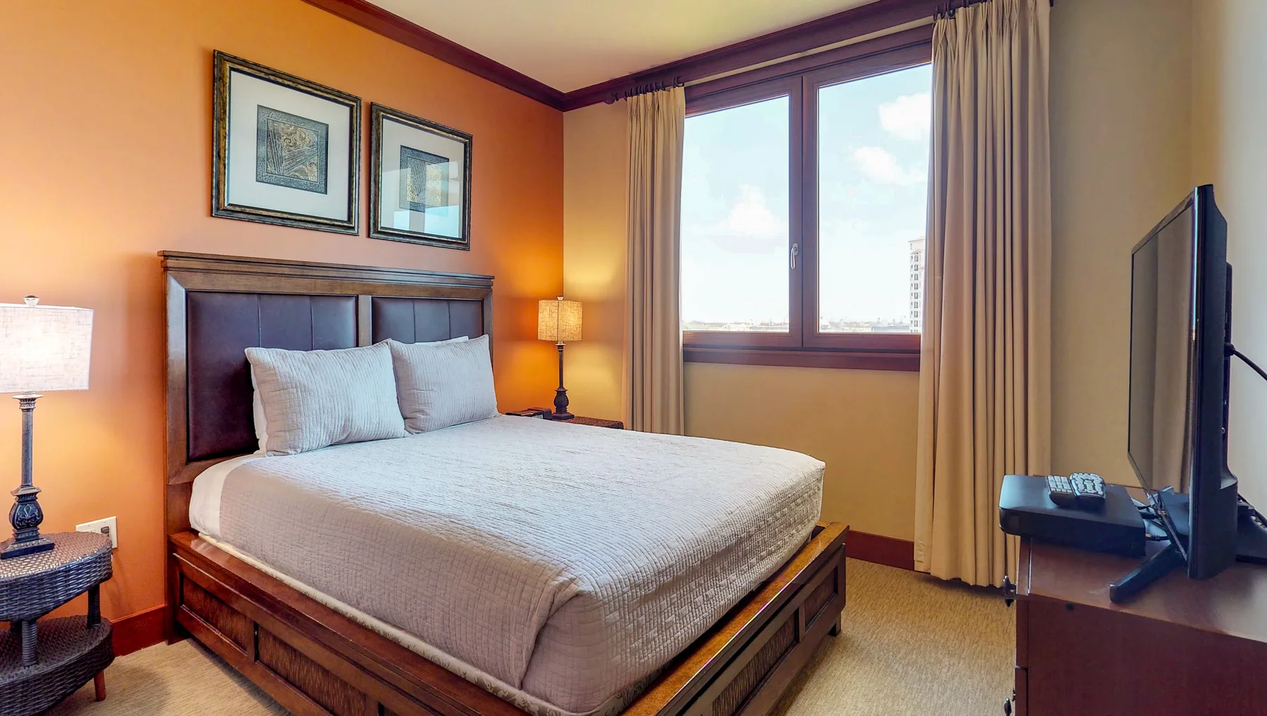 A bedroom with a large bed, framed pictures, and a window.