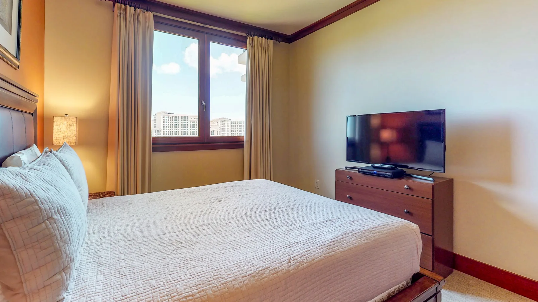 A bedroom with a bed, a television on a dresser, and a curtained window.