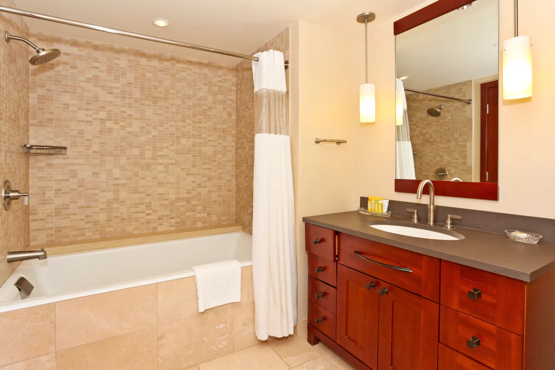 A bathroom with a bathtub, shower curtain, and vanity beneath a large mirror.