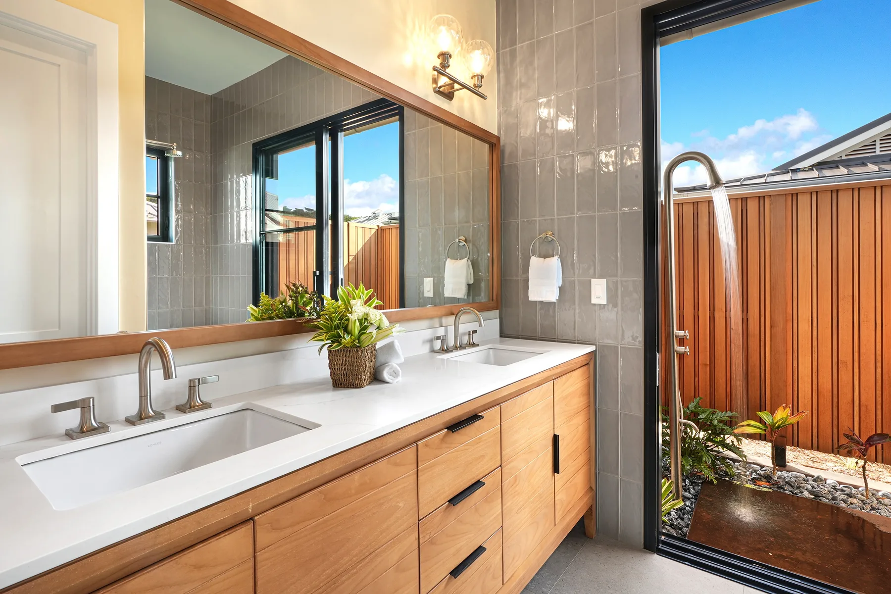 A bright bathroom with a double vanity and an open doorway to a small patio.