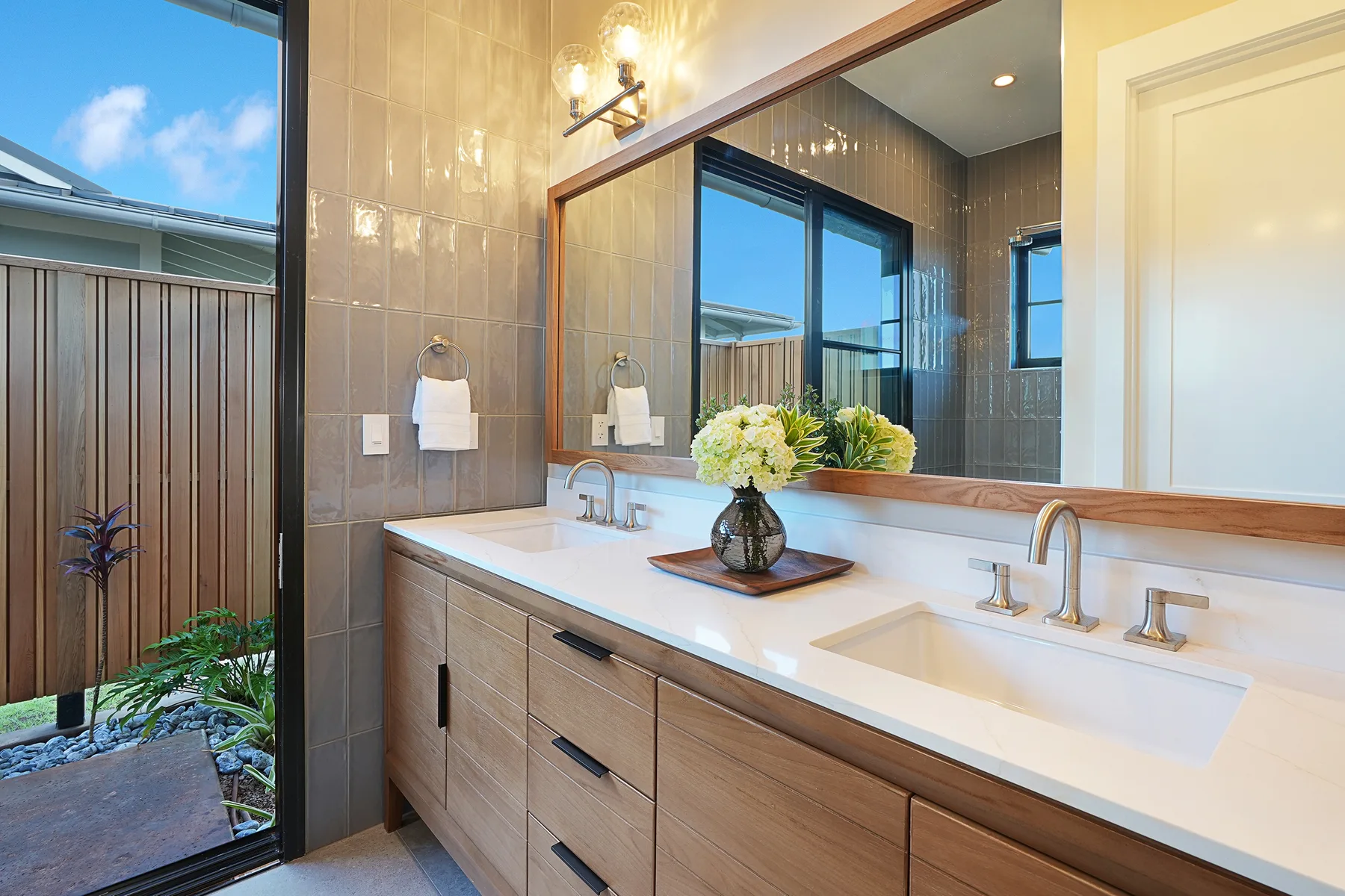 A bathroom vanity with two sinks and a large mirror beside a window.