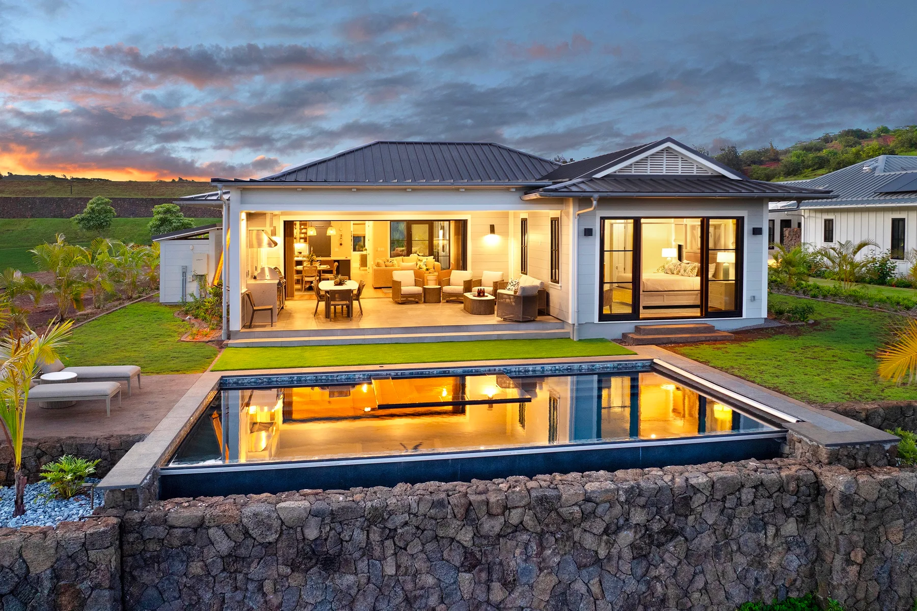 Una casa moderna da a un patio iluminado junto a una piscina rectangular al atardecer.