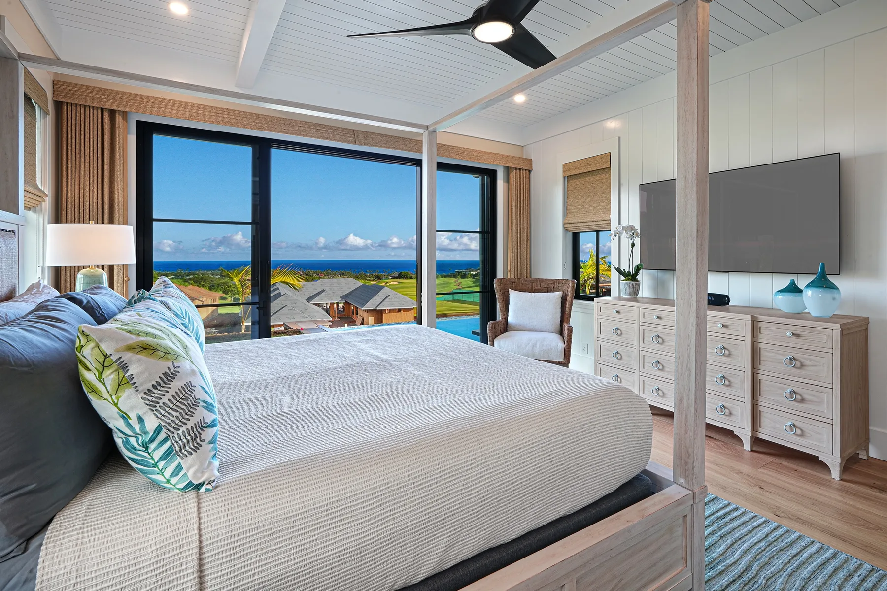 A bright bedroom with a large bed facing windows overlooking the ocean.
