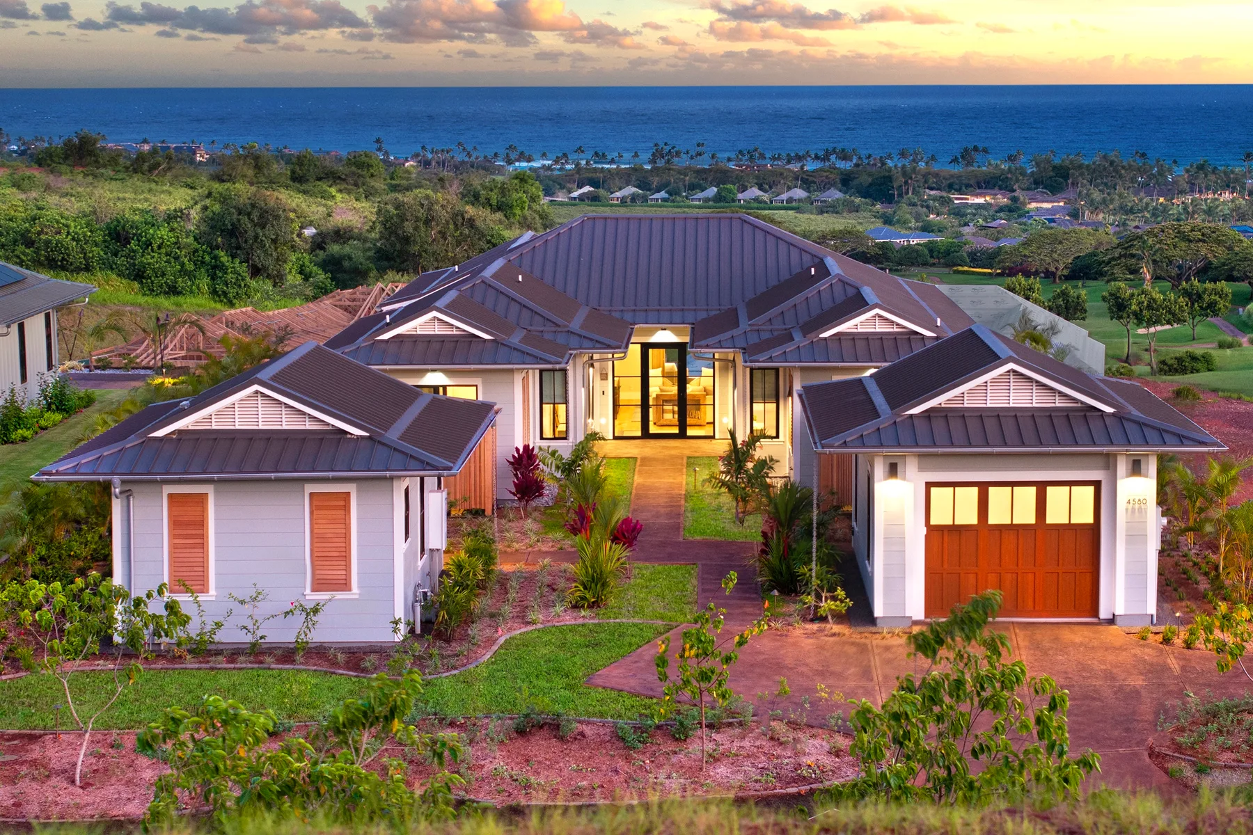 A large house with several roofed sections sits amid landscaped grounds overlooking the ocean.