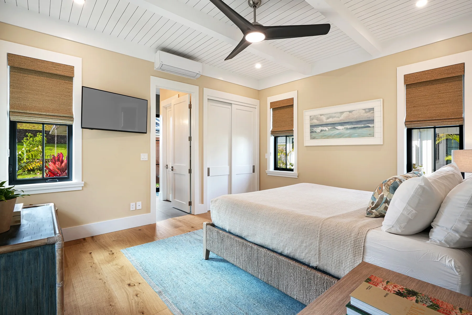 A bedroom with a large bed, a blue rug, and windows.