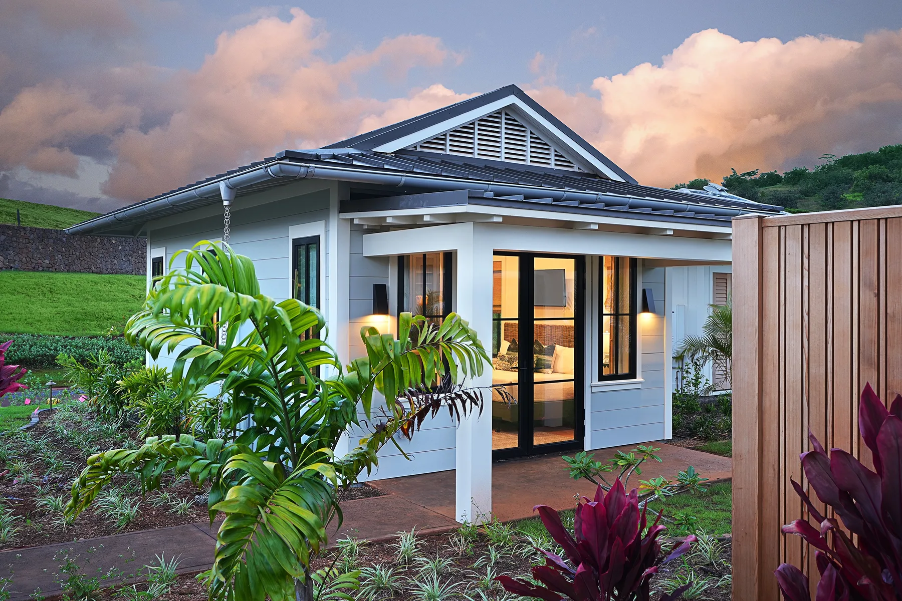 A modern house stands beside a garden, with a wooden fence in the foreground.