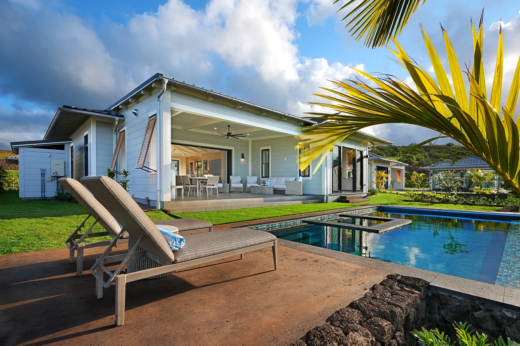 A modern house opens onto a swimming pool, with lounge seating on the patio.