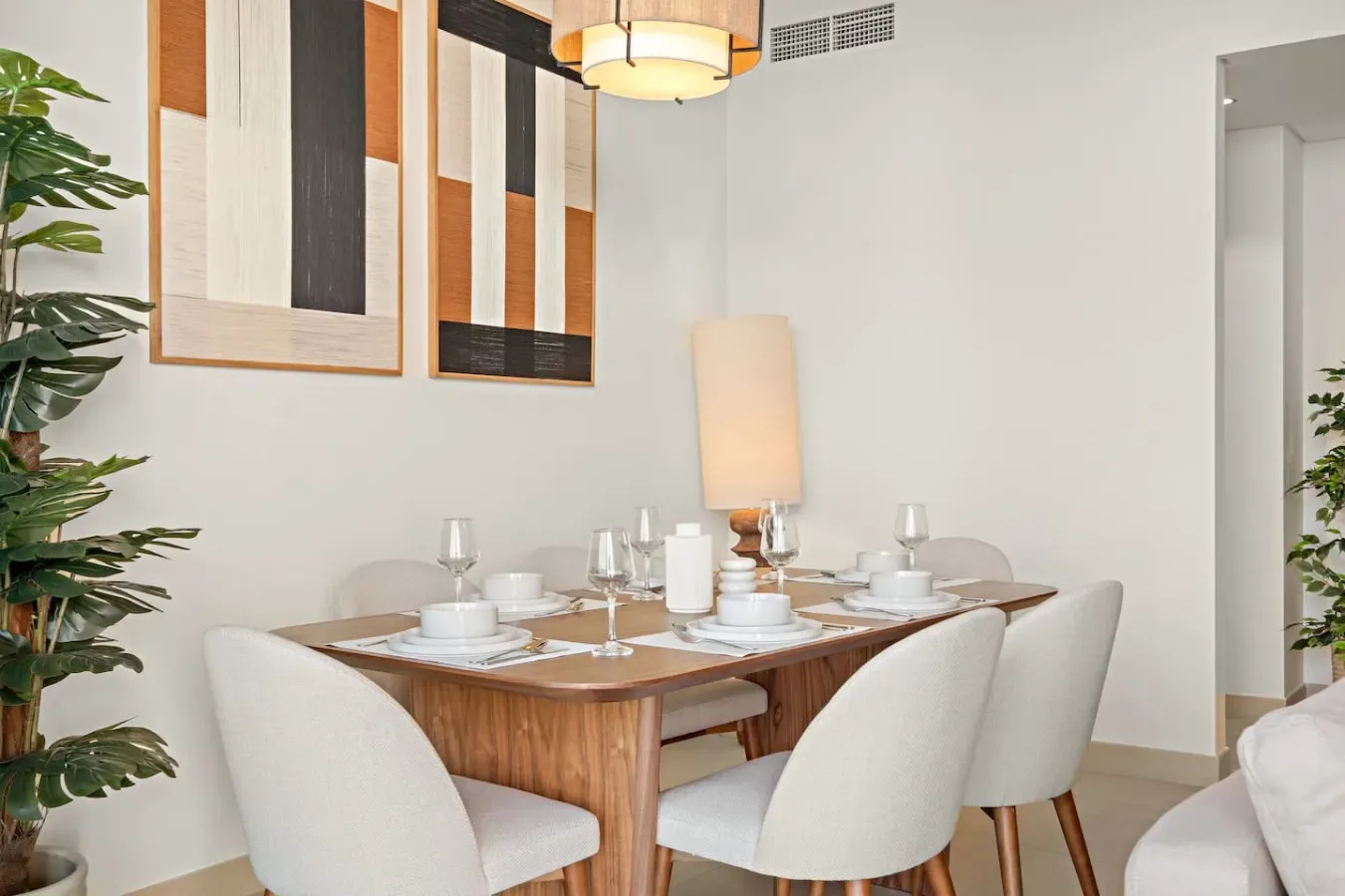 Comedor con la mesa puesta y asientos tapizados bajo cuadros abstractos.
