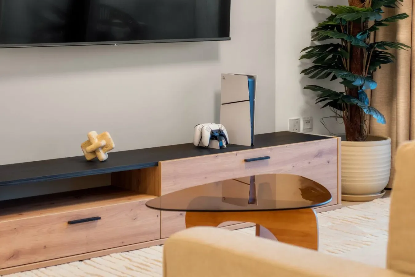 Un mueble de sala está debajo de un televisor montado en la pared, junto a una planta en maceta.