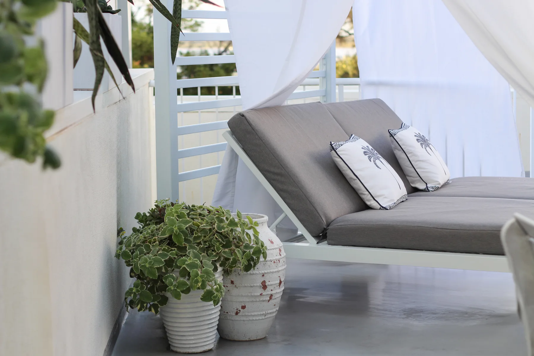 Una zona exterior de descanso con cortinas, cojines y plantas en macetas.
