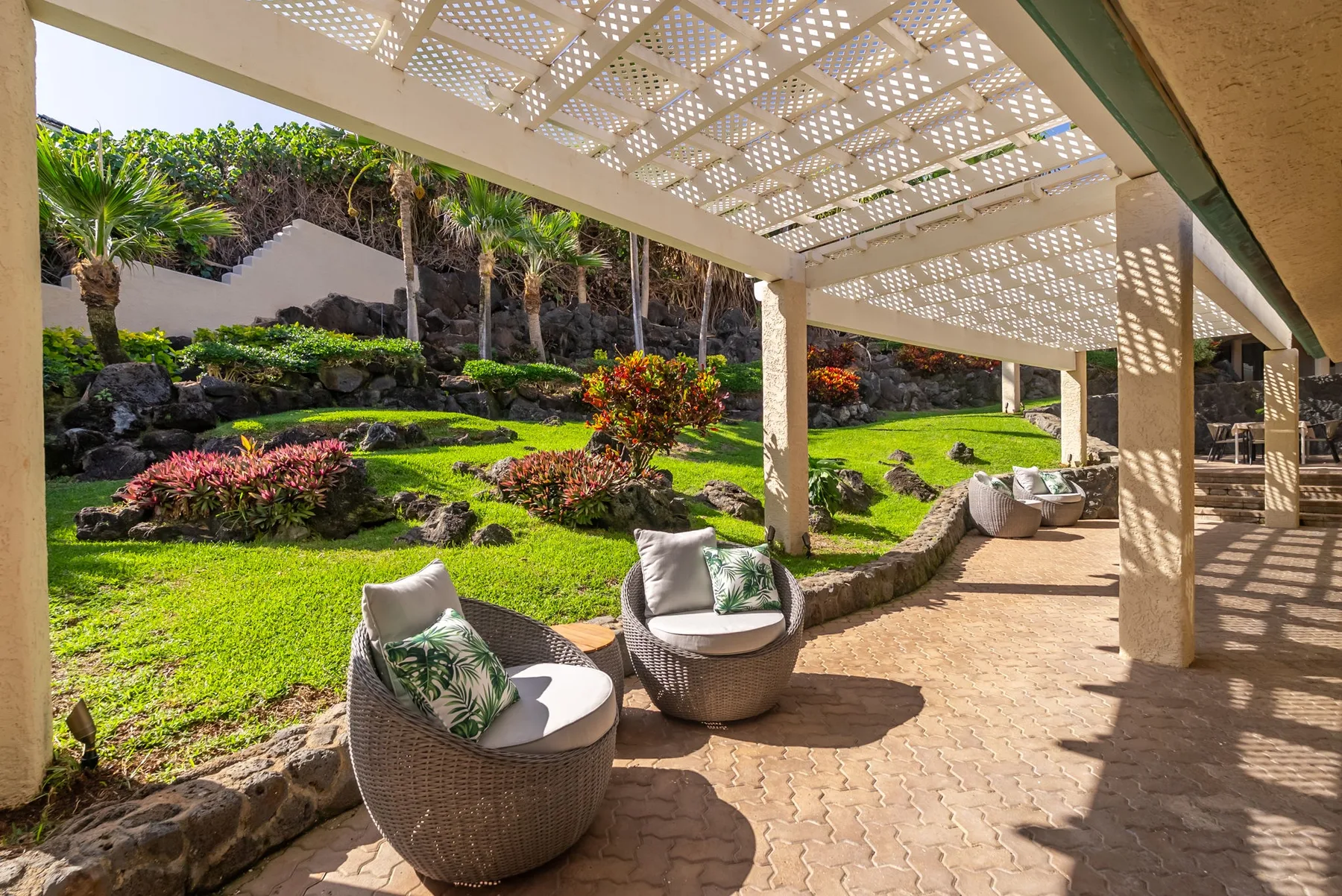 A shaded patio with outdoor seating overlooks a landscaped garden.