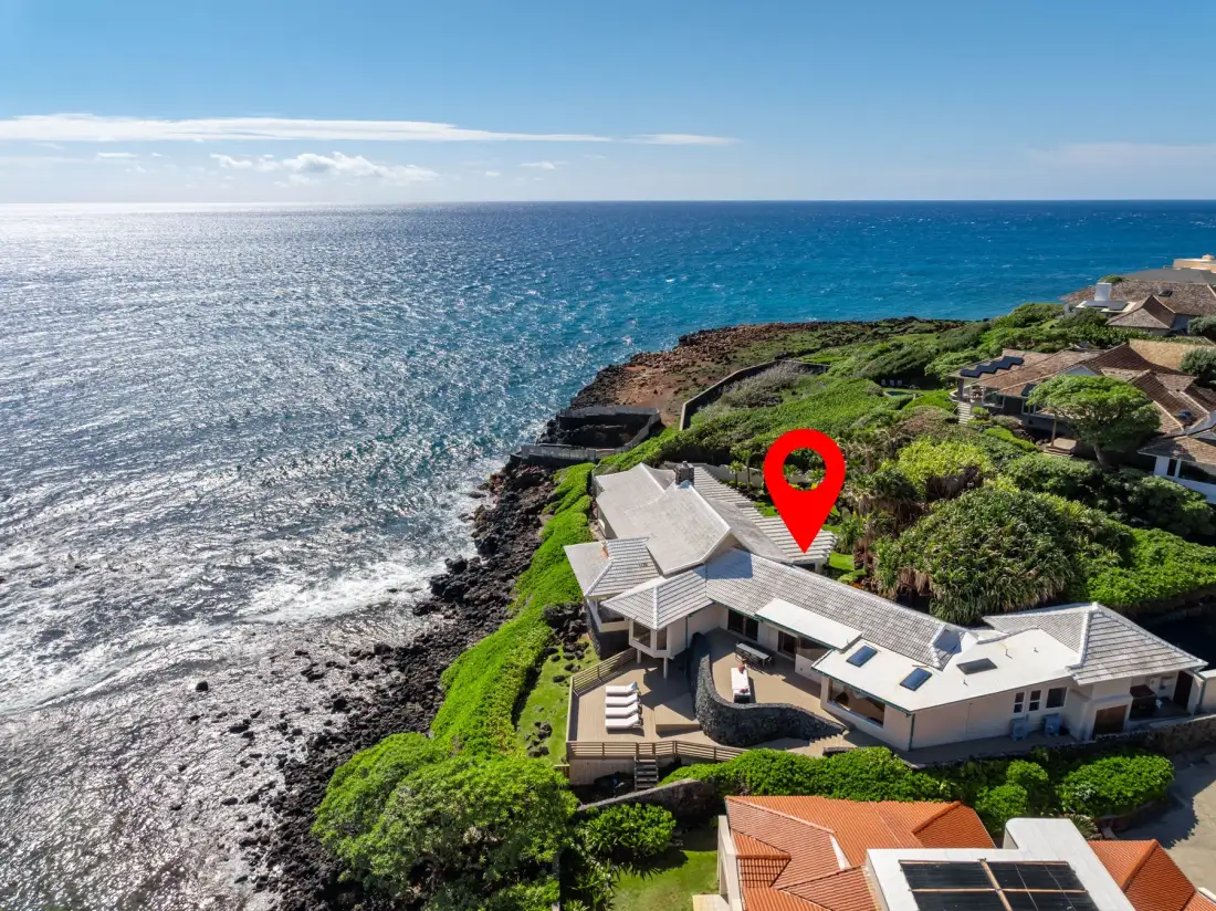 Aerial view of a coastal home beside the ocean and rocky shoreline.