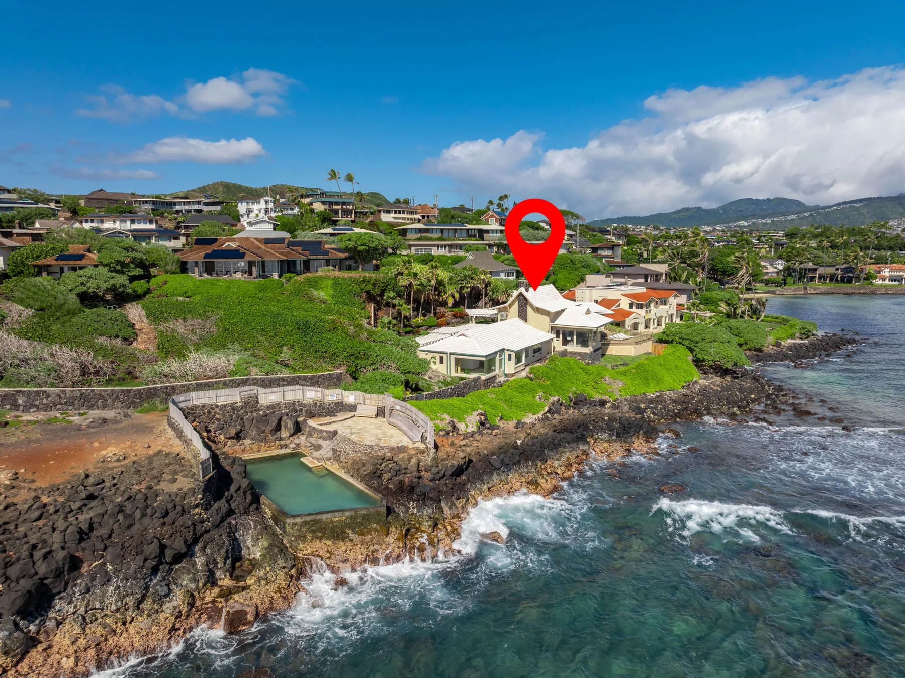 Coastal homes sit above a rocky shoreline, with a red location marker.